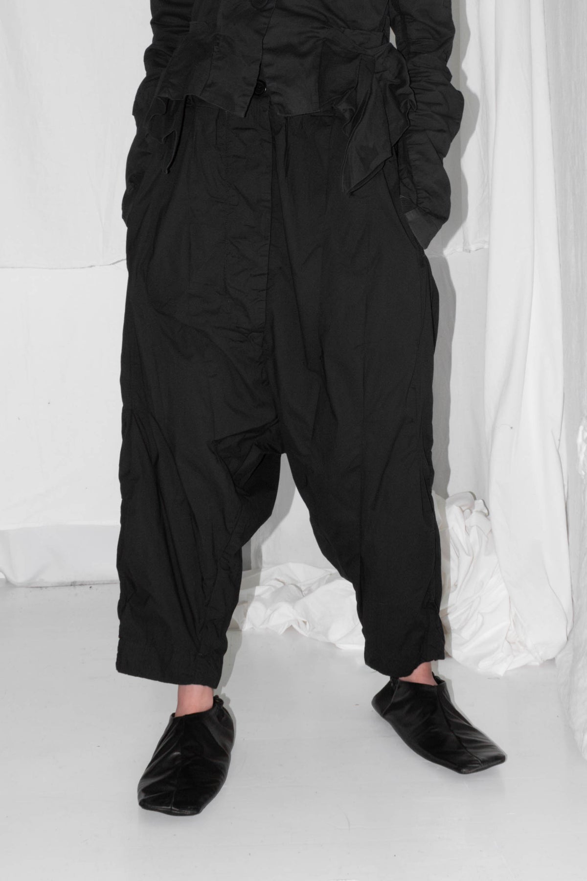 Black pleated trousers worn with leather shoes, showing dropped crotch silhouette and cropped length – Cropped Pleat Light Trousers by NELLY JOHANSSON