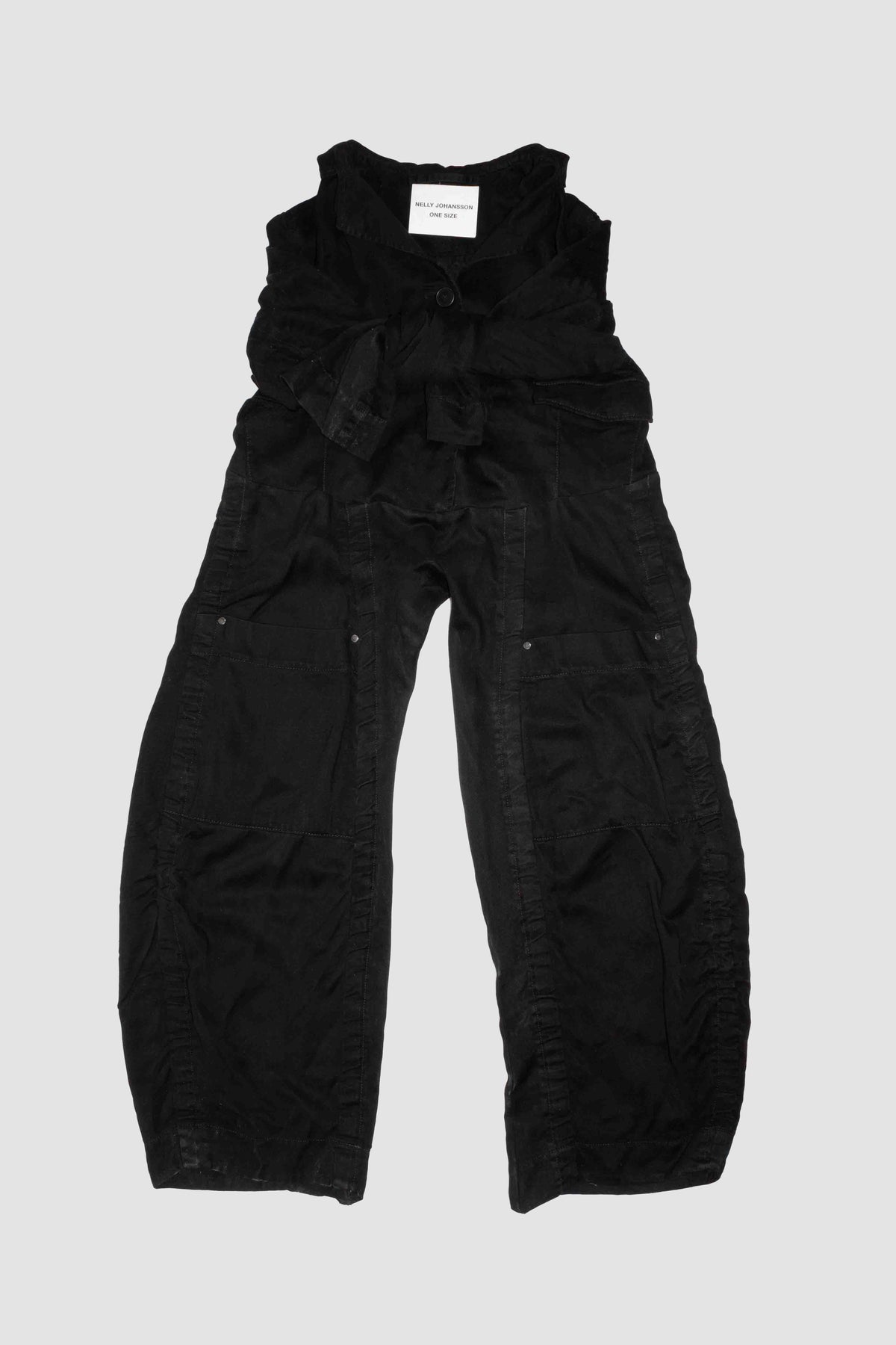 Black deconstructed trousers laid flat without sleeves, showing wide leg silhouette and button fastening – Deconstructed Lyocell Trousers by NELLY JOHANSSON