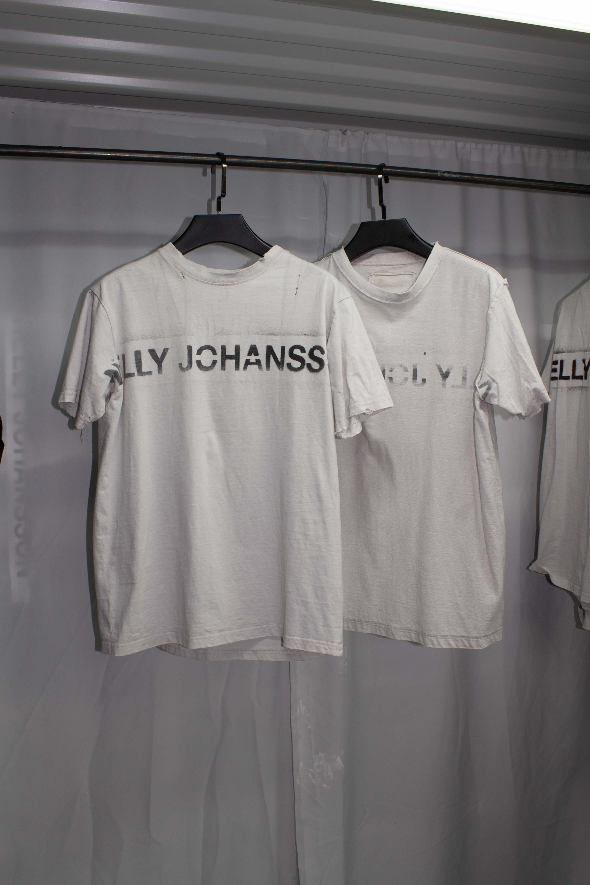 Multiple white t-shirts with NELLY JOHANSSON prints hanging on clothing rail
