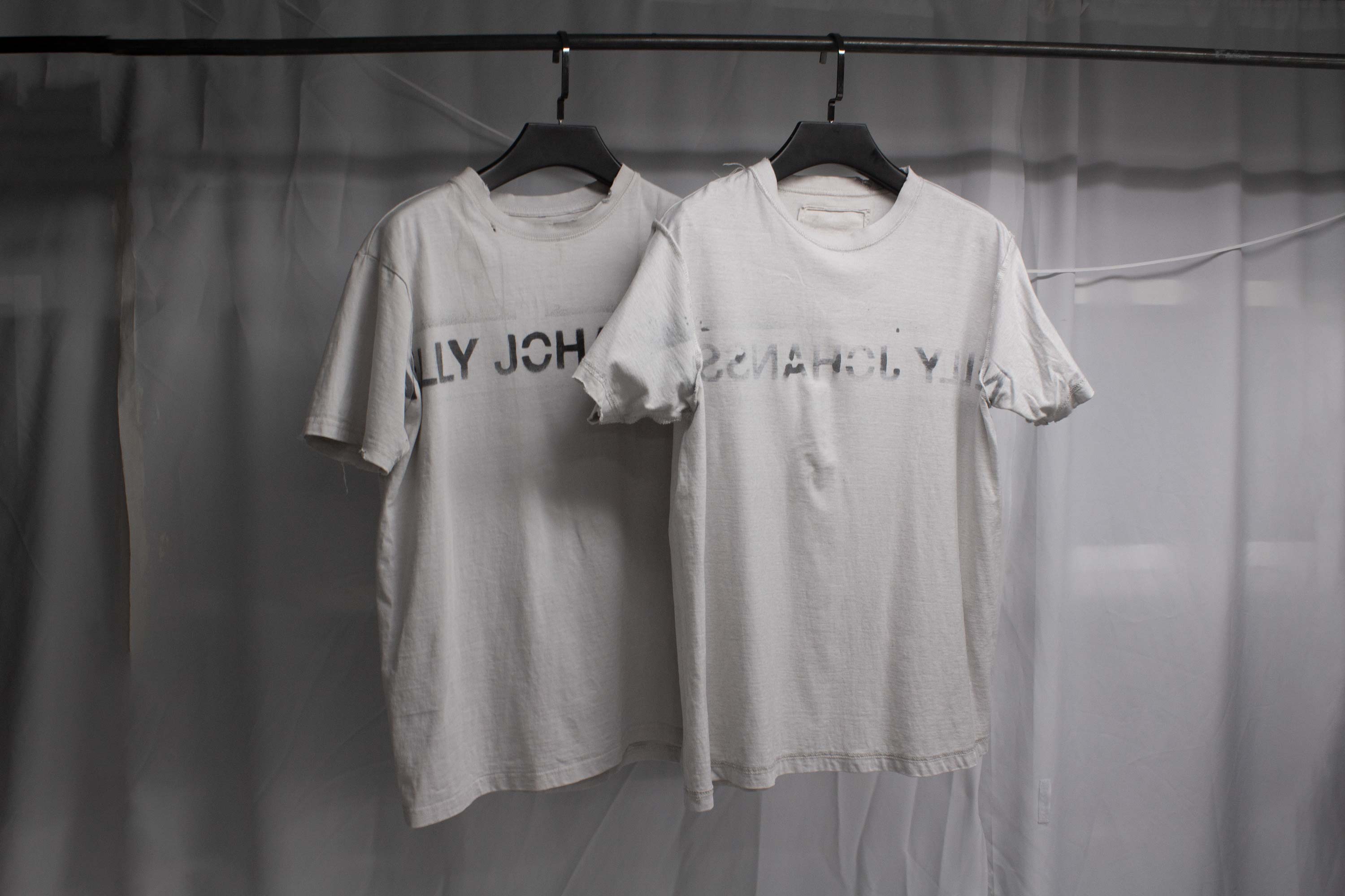 Two white cotton t-shirts hanging on hangers showing NELLY JOHANSSON text print