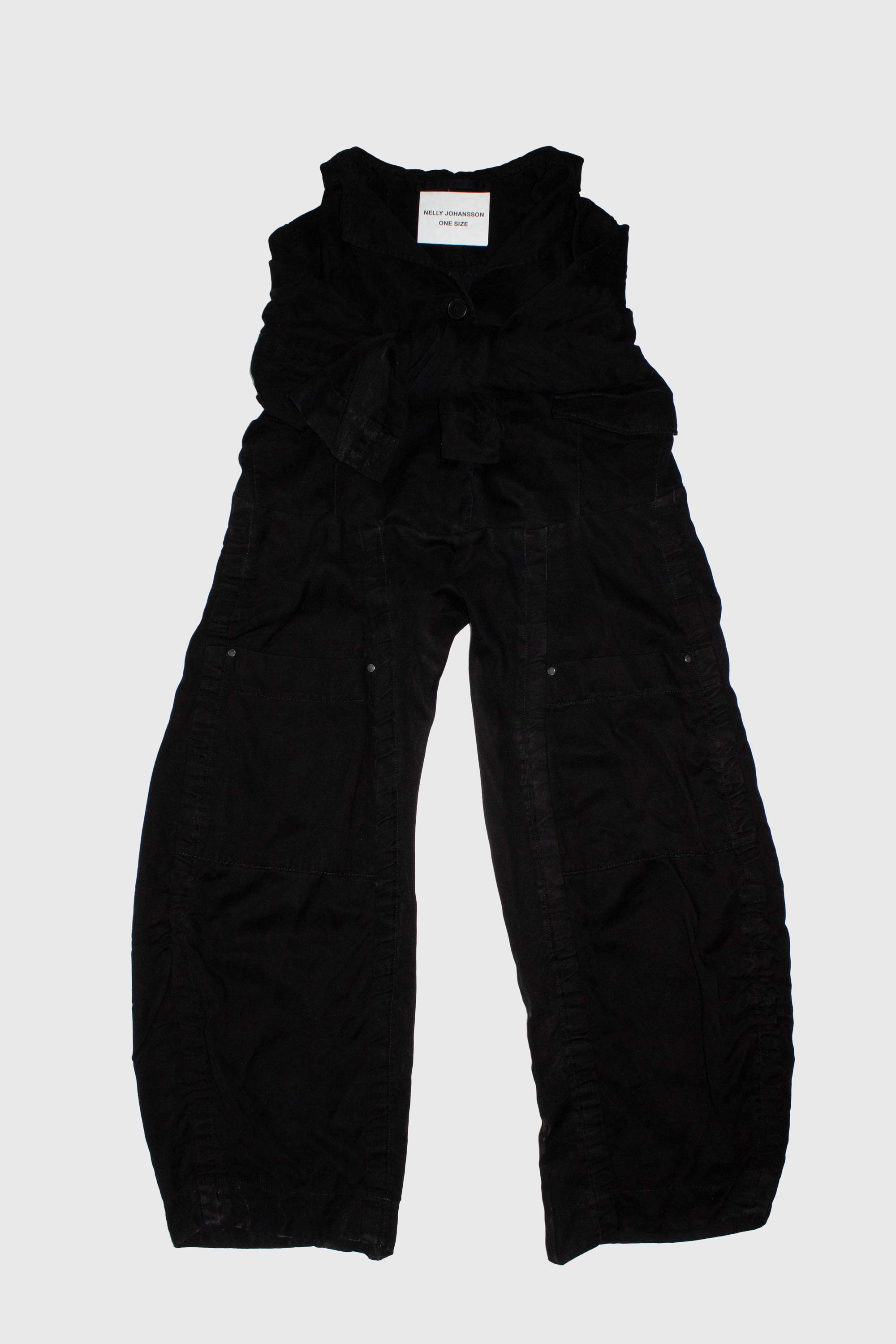 Black deconstructed trousers laid flat without sleeves, showing wide leg silhouette and button fastening