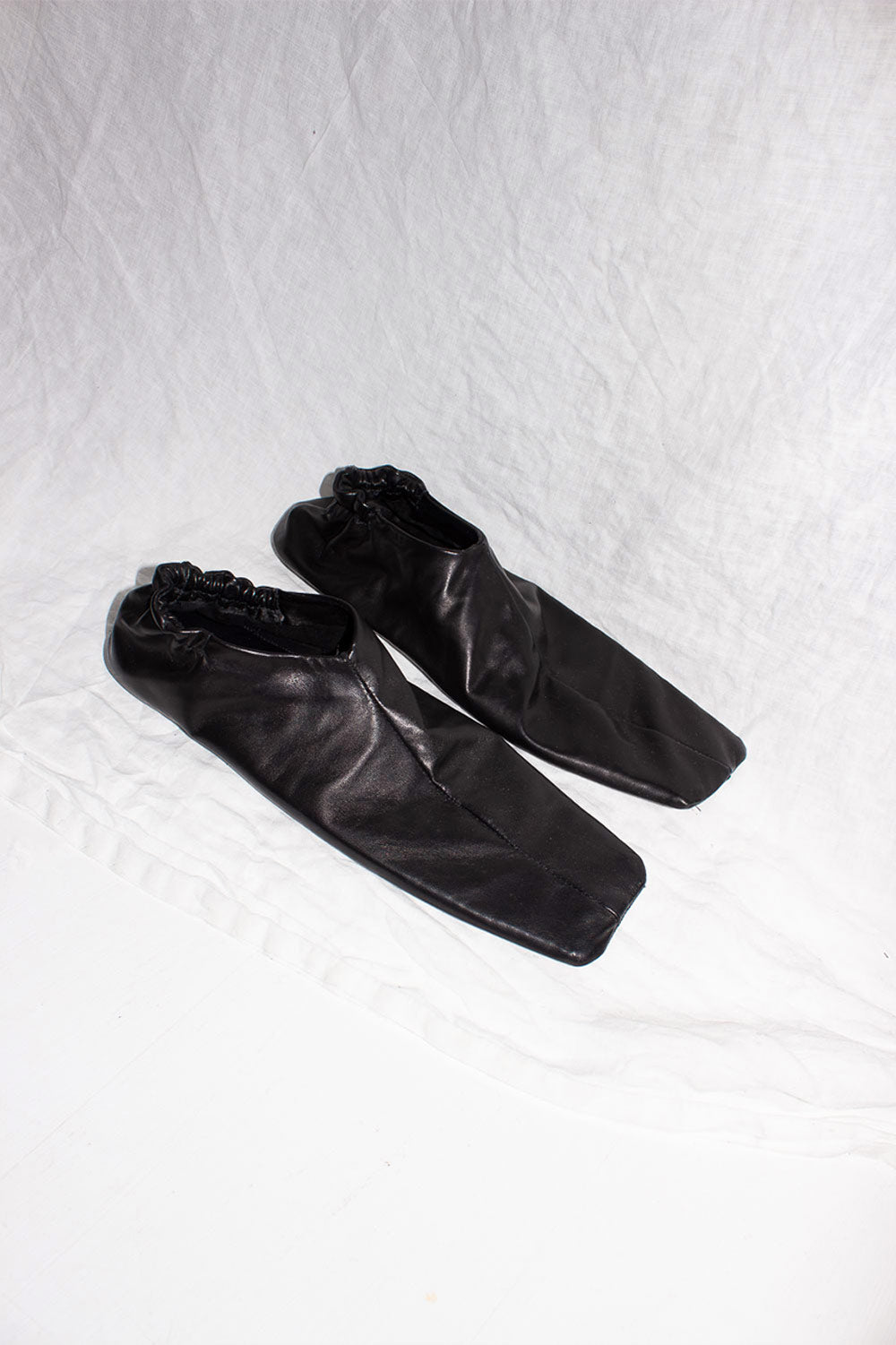 Pair of black horse leather slip-on shoes with square toes, overhead view on white fabric