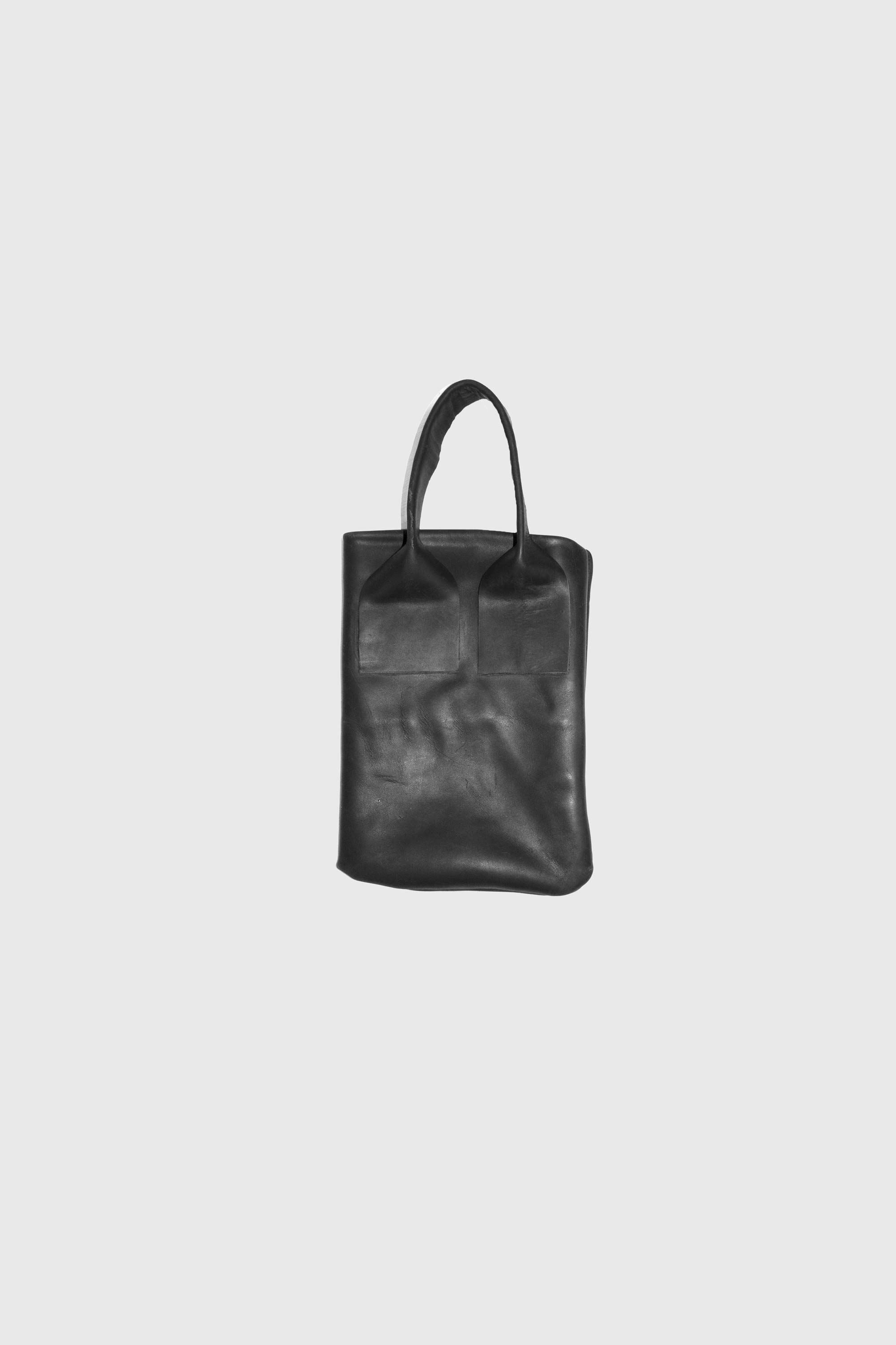 Black rectangular leather tote with single top handle against light grey background