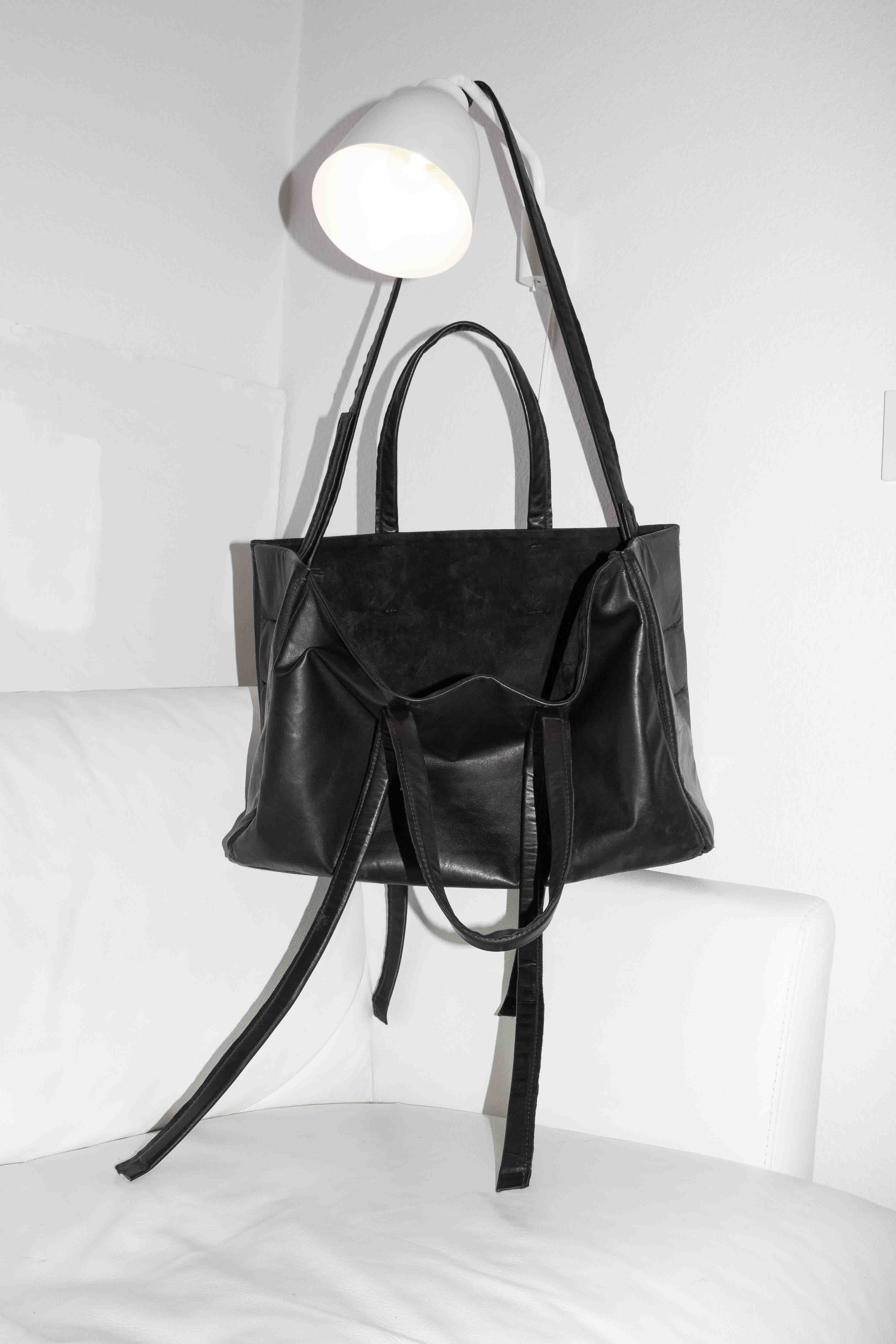 Black horse leather tote bag on white chair showing structured silhouette with dual handles and shoulder strap