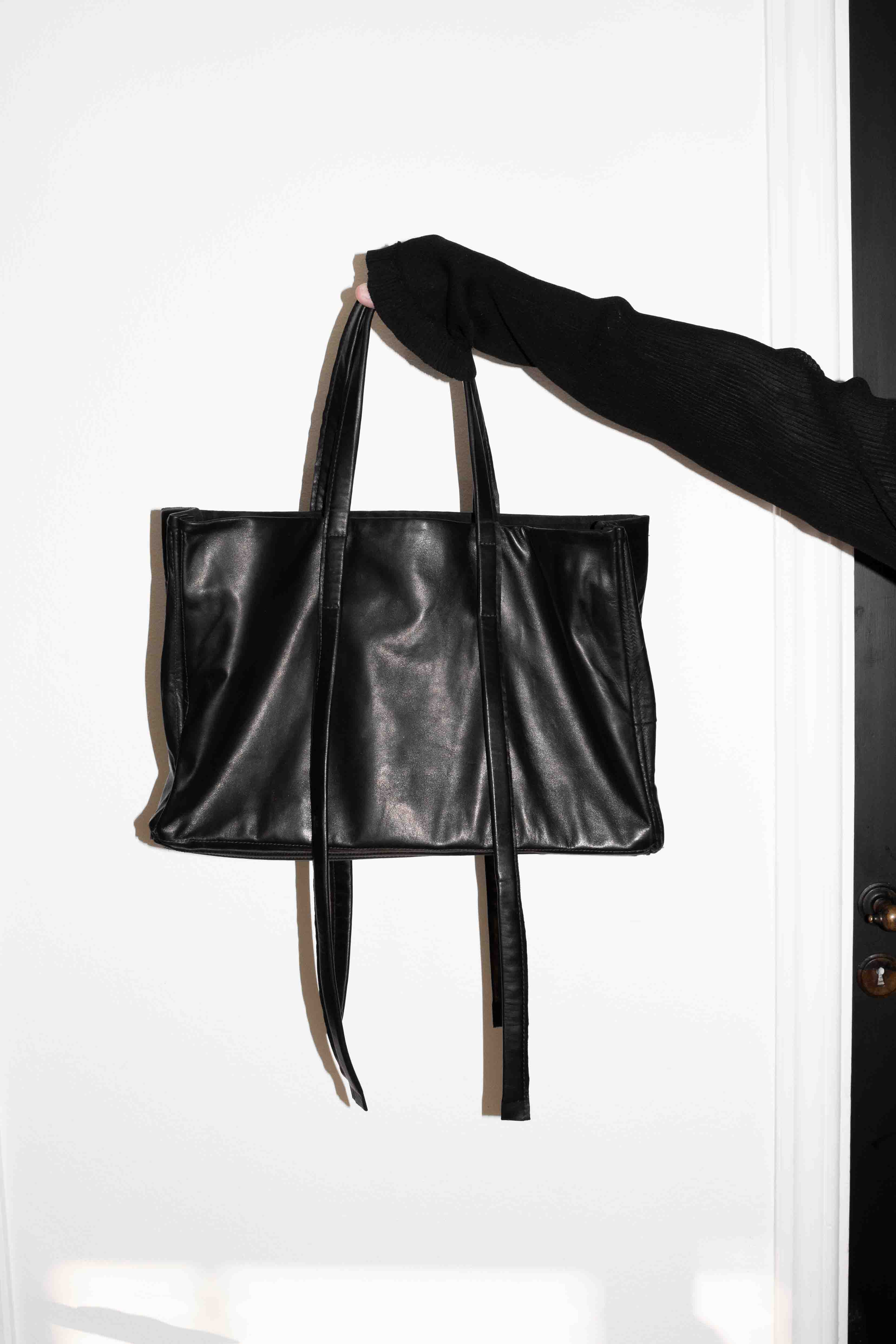 Black horse leather tote bag carried by extended arm showing smooth leather exterior and proportions