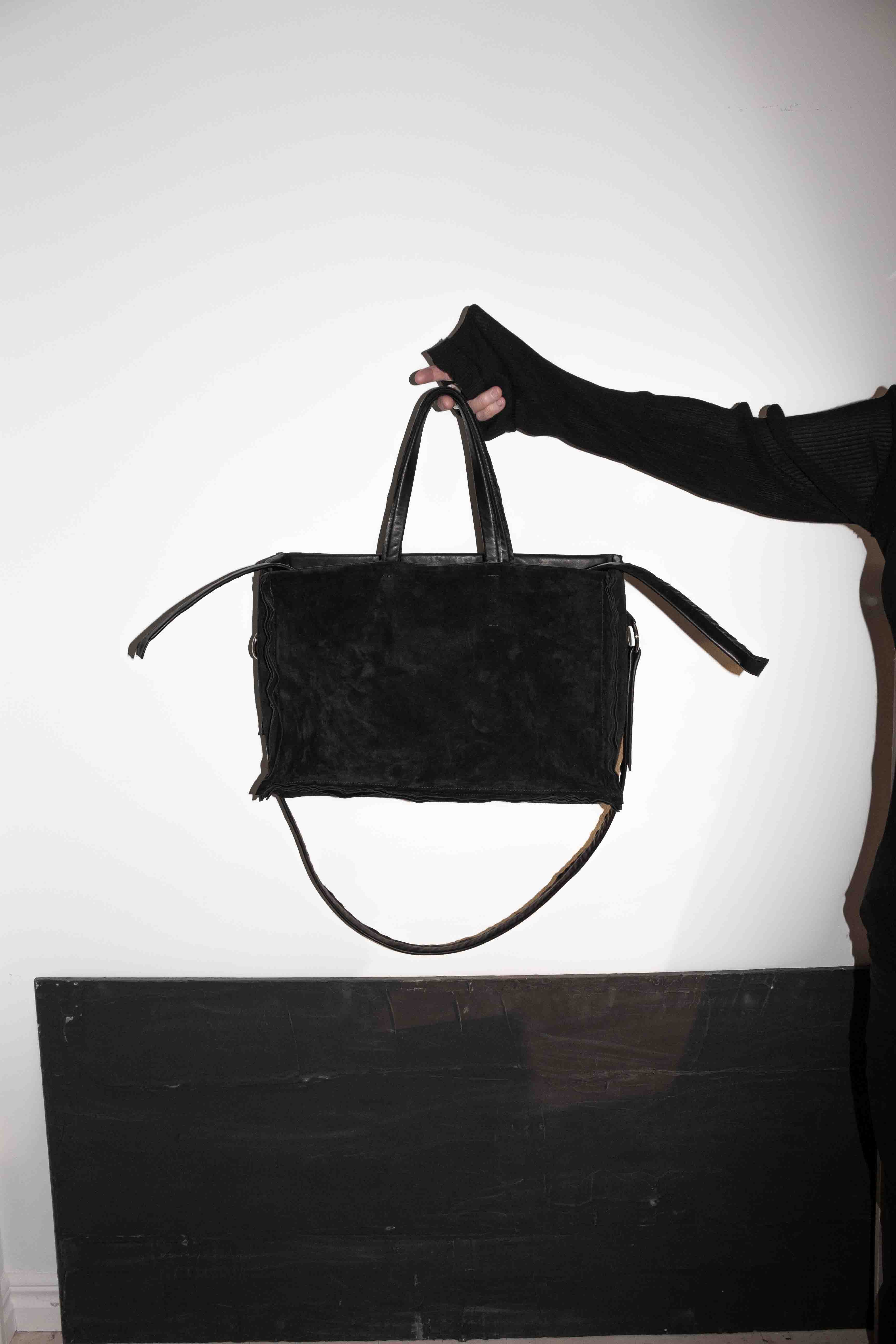 Hand carrying black horse leather tote bag demonstrating grip and handle positioning