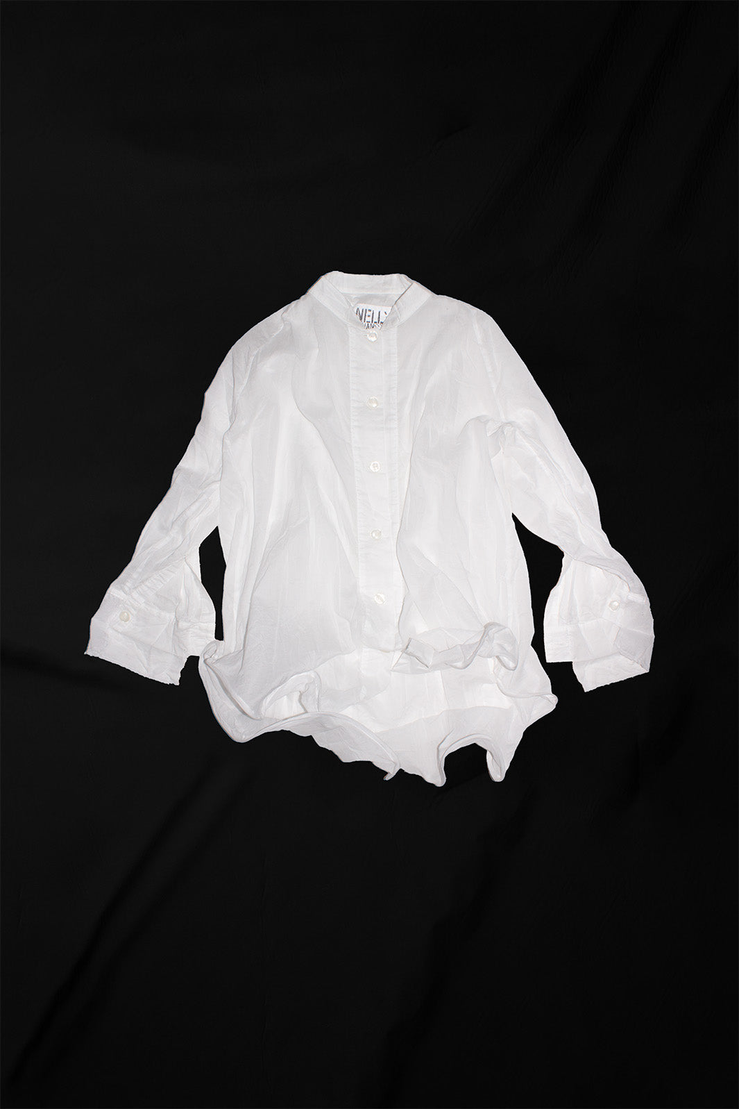 White oversized shirt on black background showing mandarin collar and sculptural proportions