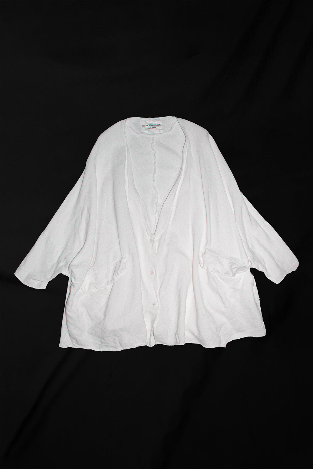 White oversized cardigan laid flat showing full length with button front closure and patch pockets