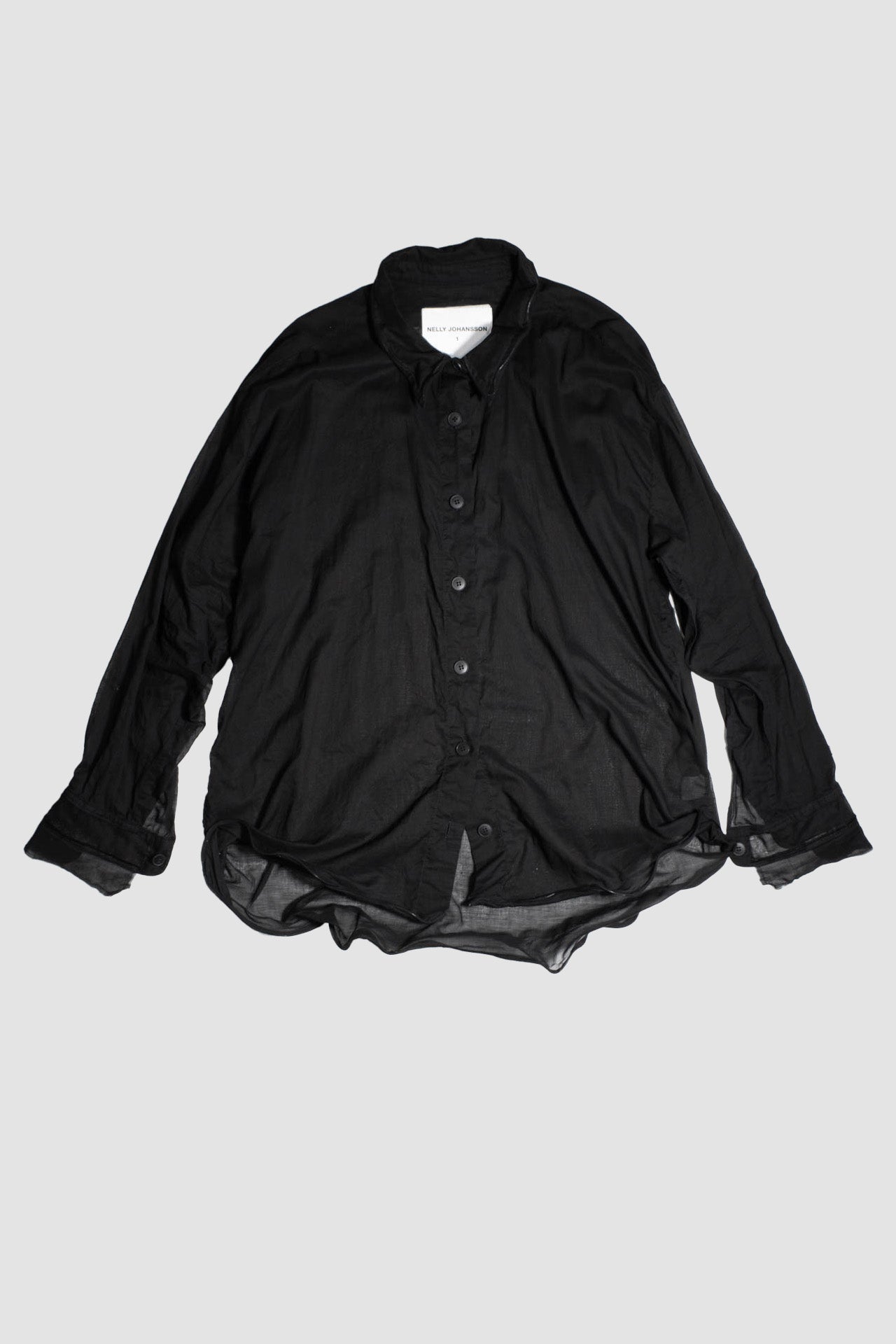 Black cotton shirt laid flat showing full silhouette, button front, and Nelly Johansson label
