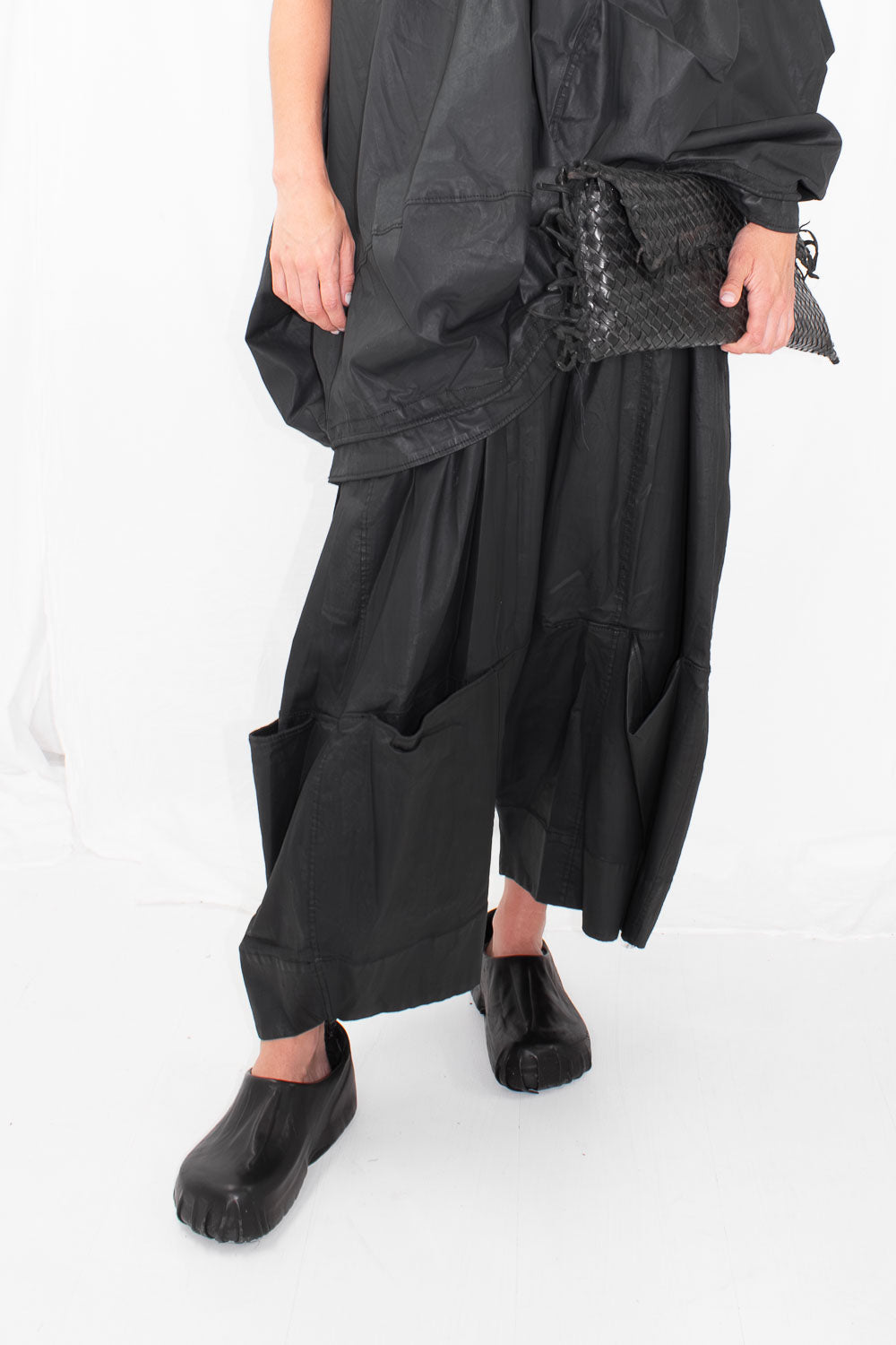 Model wearing black drop crotch trousers with large angled pockets, holding black woven clutch
