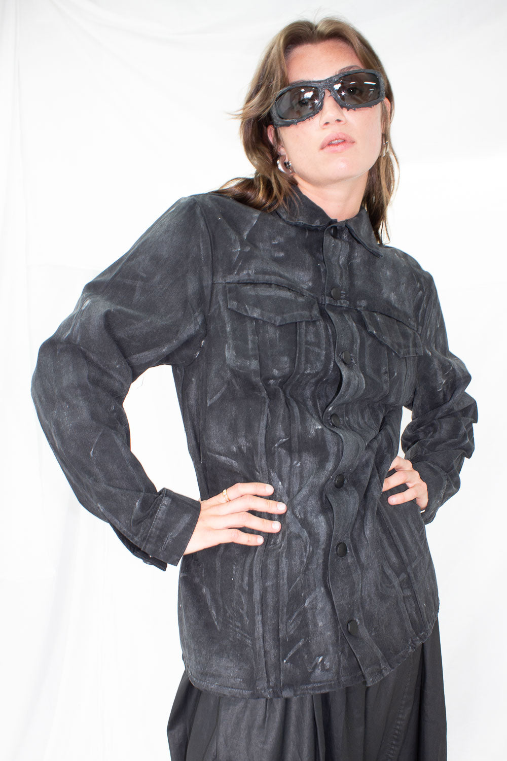 Model wearing black waxed denim jacket with sunglasses, front view showing structured fit and chest pockets