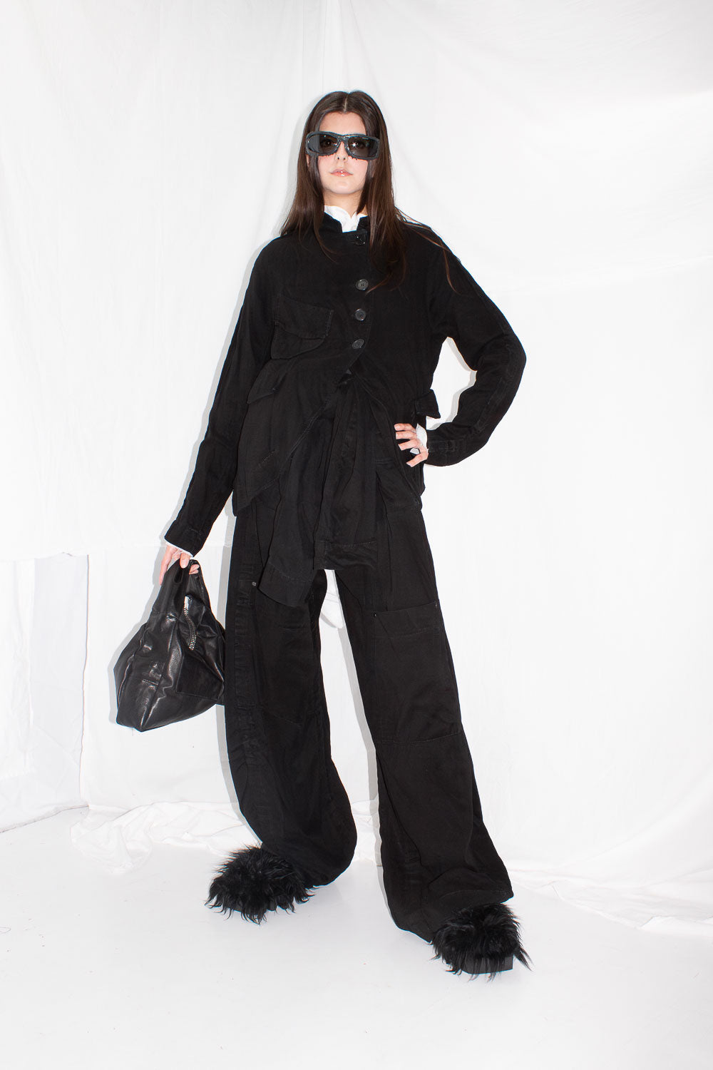 Model wearing black lyocell jacket with wide-leg trousers, feathered shoes, and sunglasses, front view