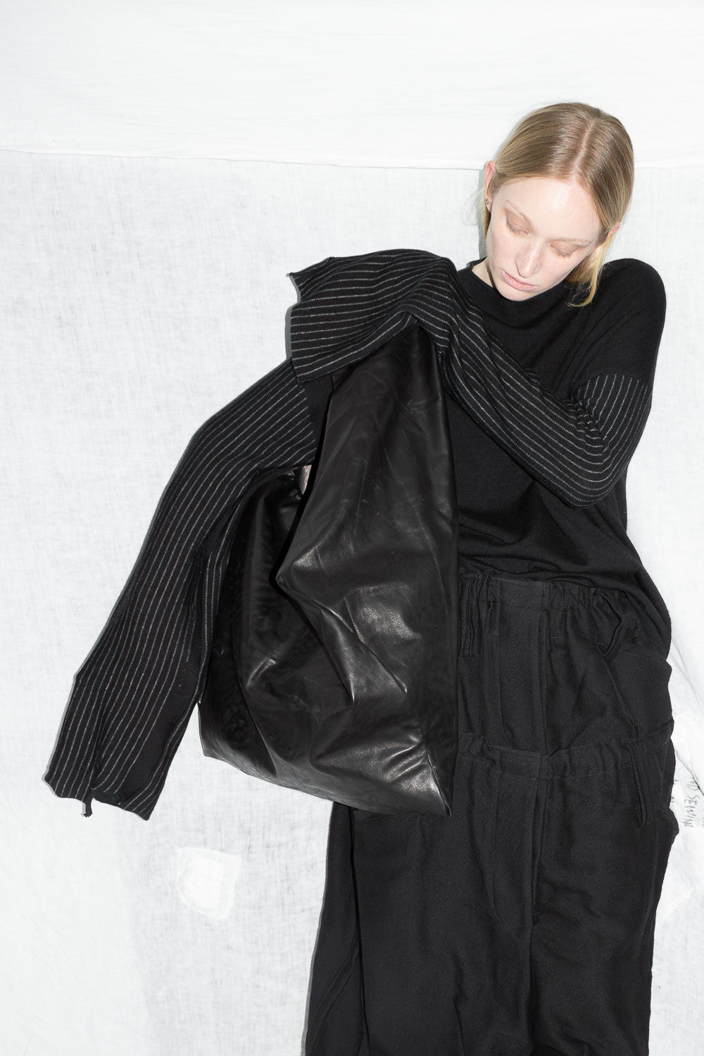 Model holding leather jacket while wearing black sweater with distinctive striped sleeves