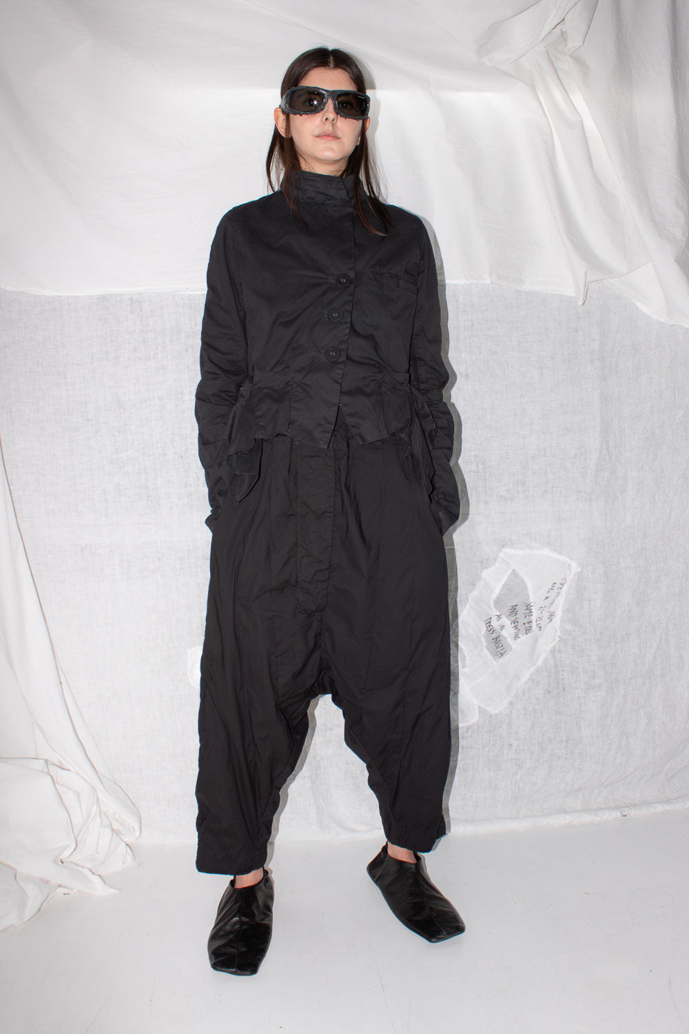 Model wearing black pleated trousers with turtleneck and sunglasses, full front view styling