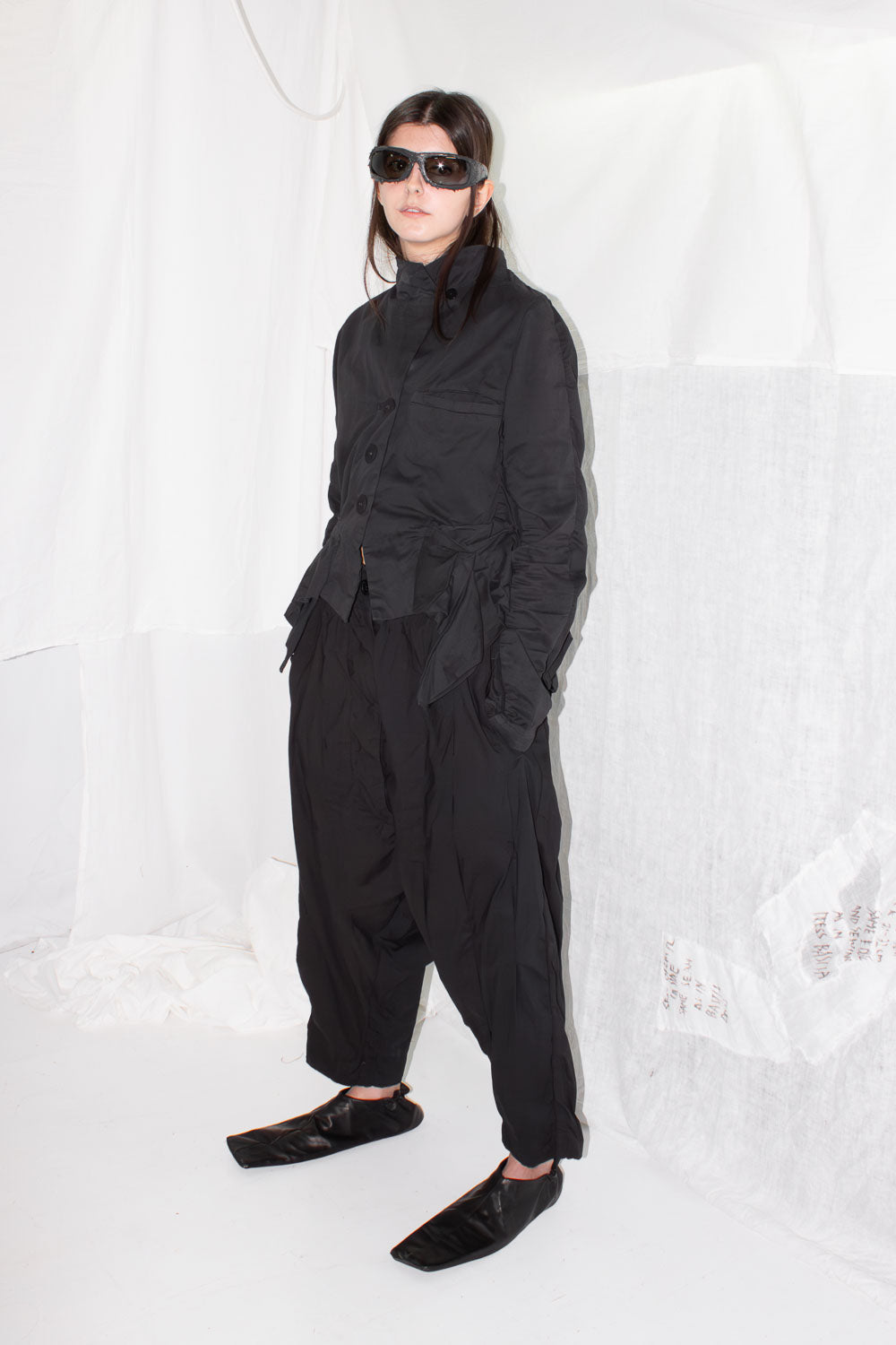 Model wearing jacket with sunglasses in full black ensemble
