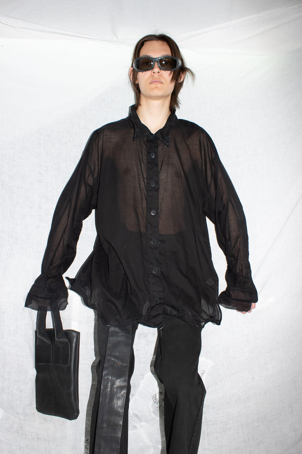 Model in sunglasses wearing black oversized shirt with leather trousers, showing complete look