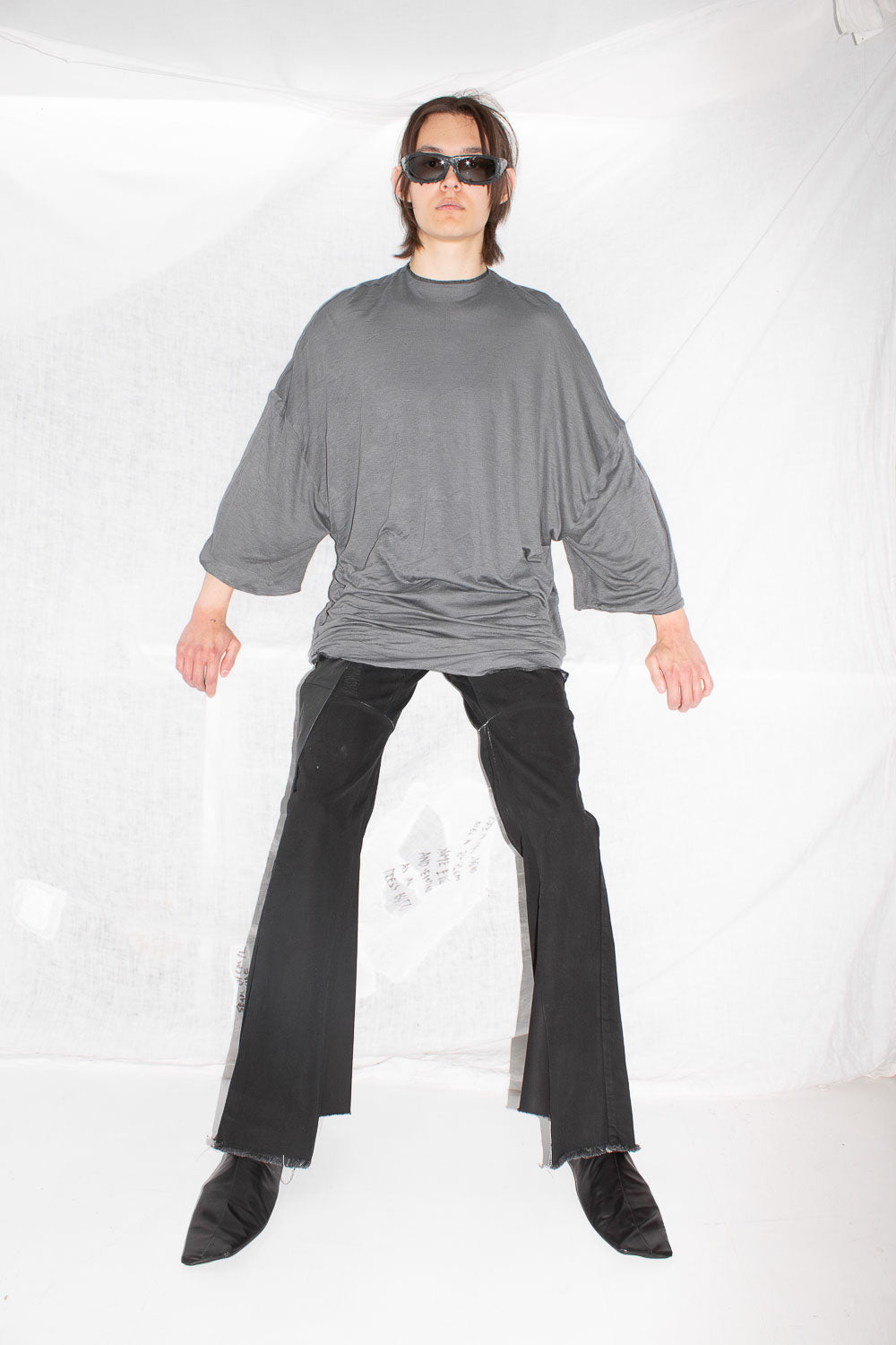 Full body shot of model wearing grey t-shirt with black leather pants, arms outstretched