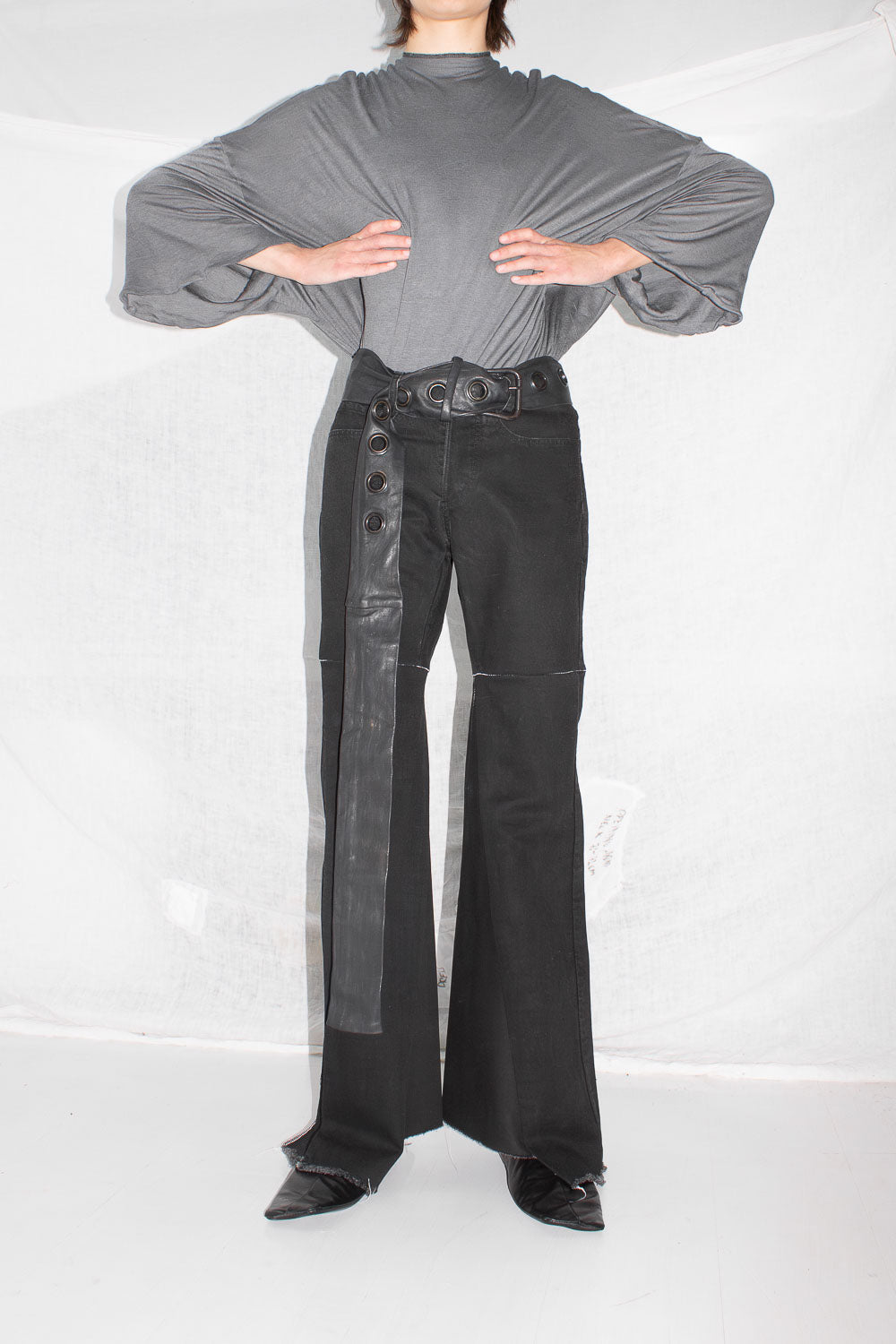 Front view of figure in gray top wearing black flared jeans with leather belt detail