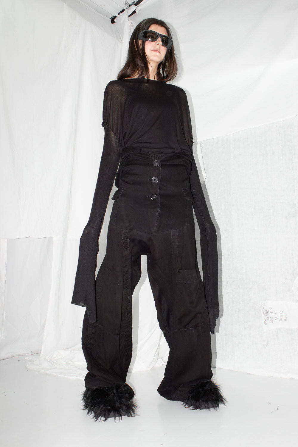 Model wearing black deconstructed trousers with sheer top, front view showing high-rise button closure