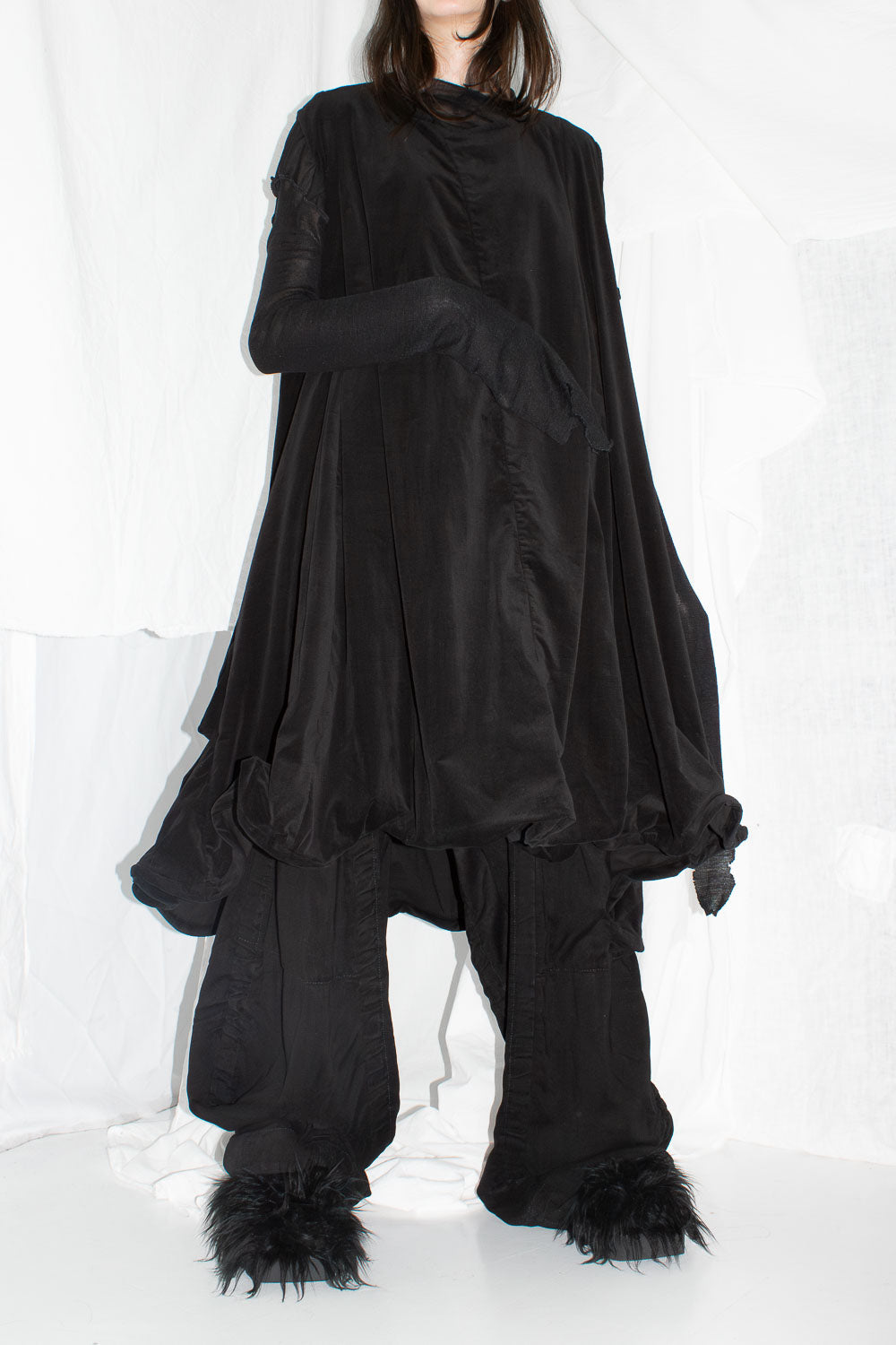Black velvet sculptural dress with wire-framed hemline worn with wide-leg trousers and fur slippers
