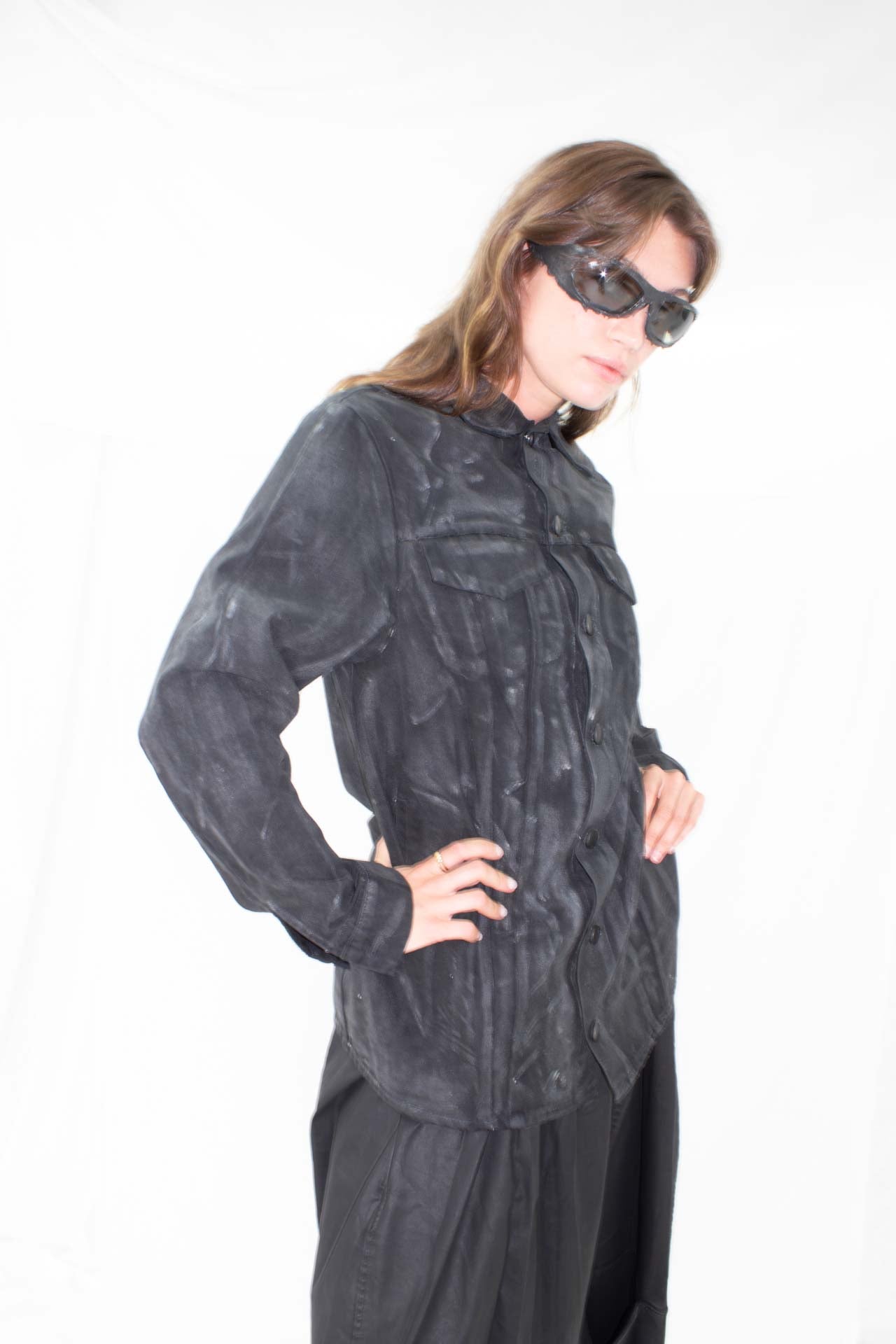 Model in black waxed denim jacket and sunglasses, side angle showing jacket silhouette and length