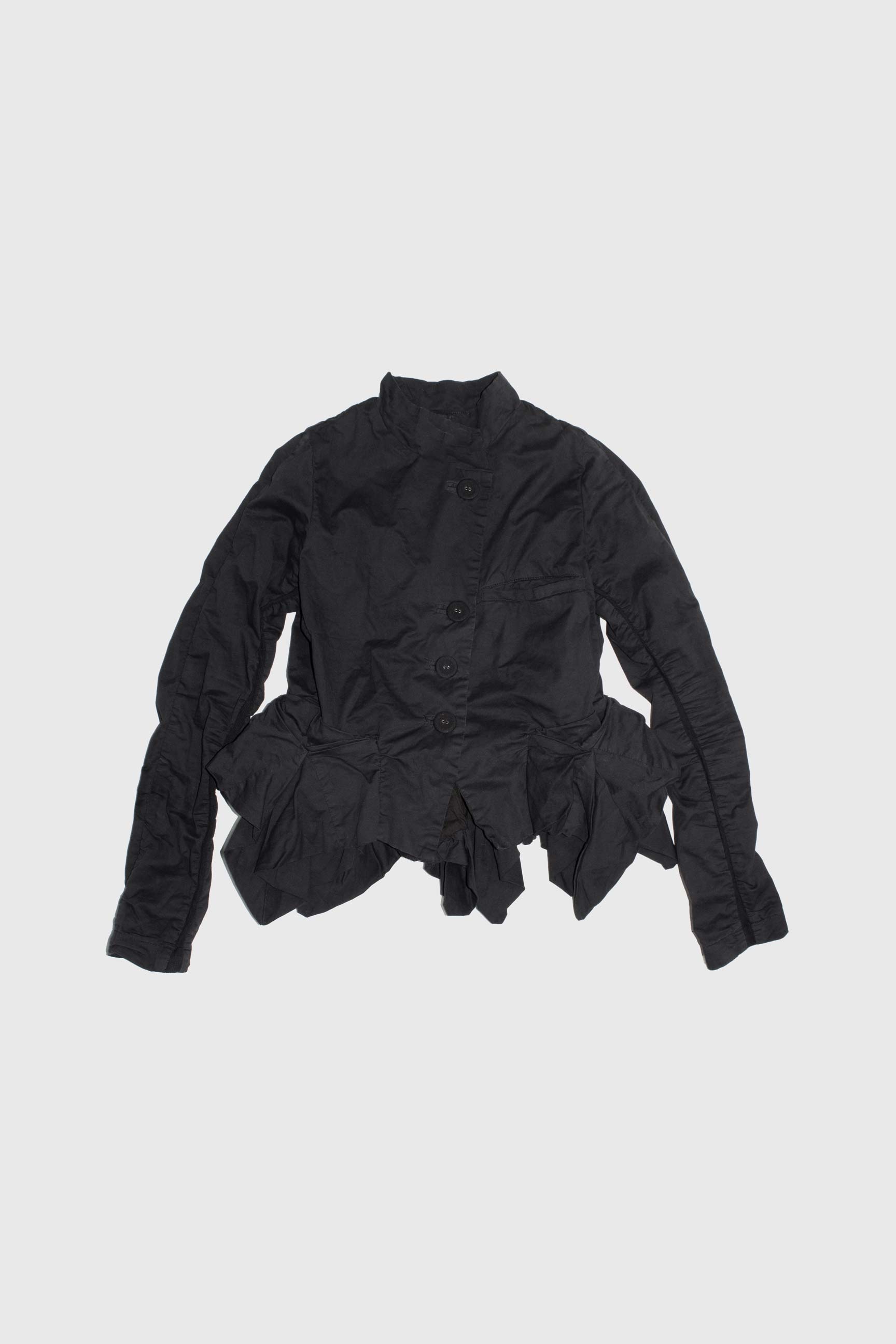 Black cotton jacket laid flat showing asymmetric button closure and ruched side details