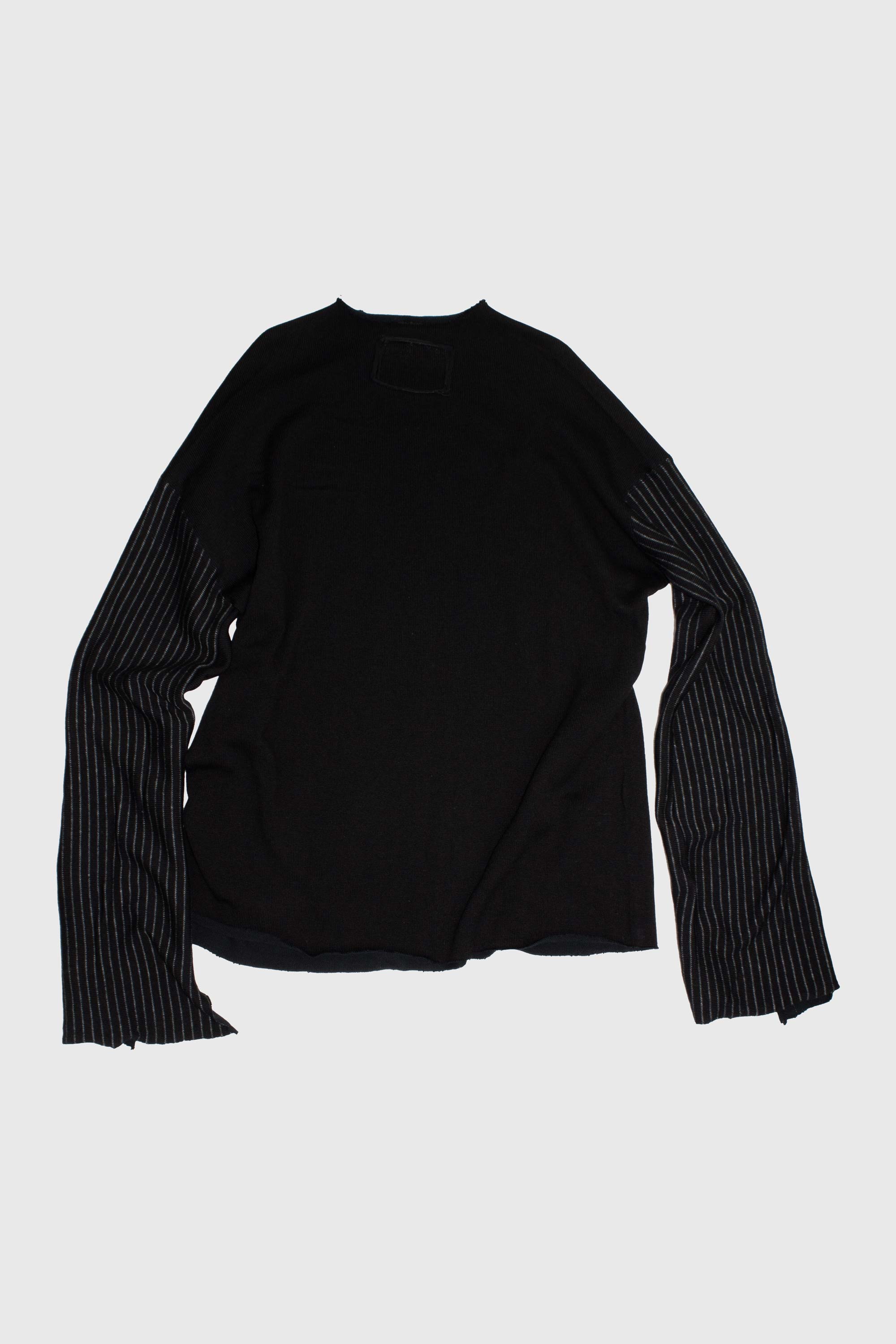 Black knit sweater flat lay showing contrasting striped sleeves and raw hem construction