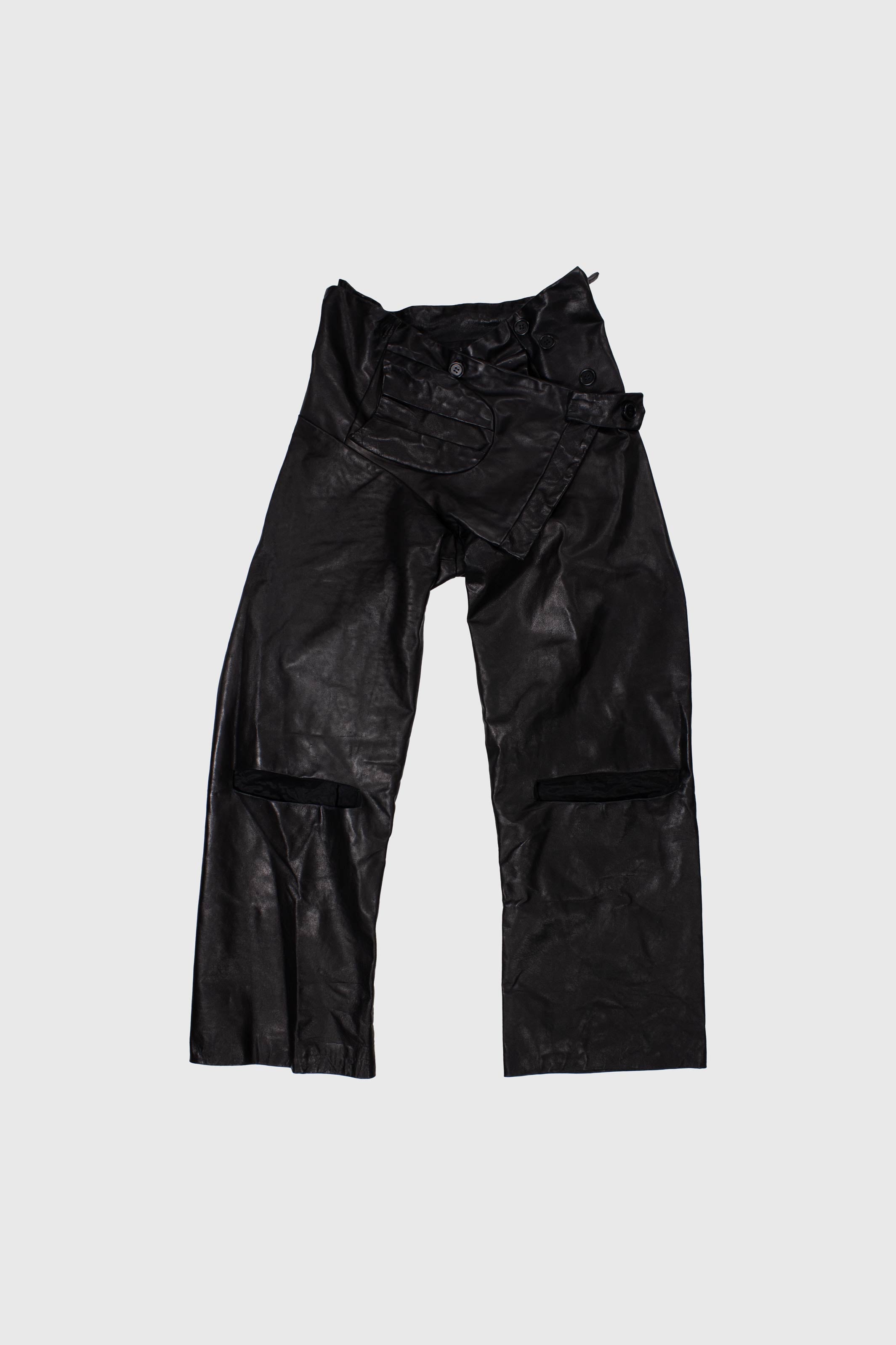 Black leather trousers laid flat showing buckle details and knee cut-outs