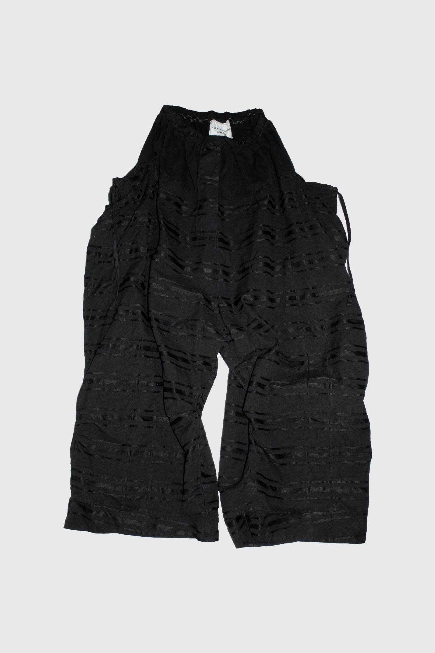 Black oversized trousers with horizontal manipulated stripes laid flat showing elastic waistband and wide leg silhouette