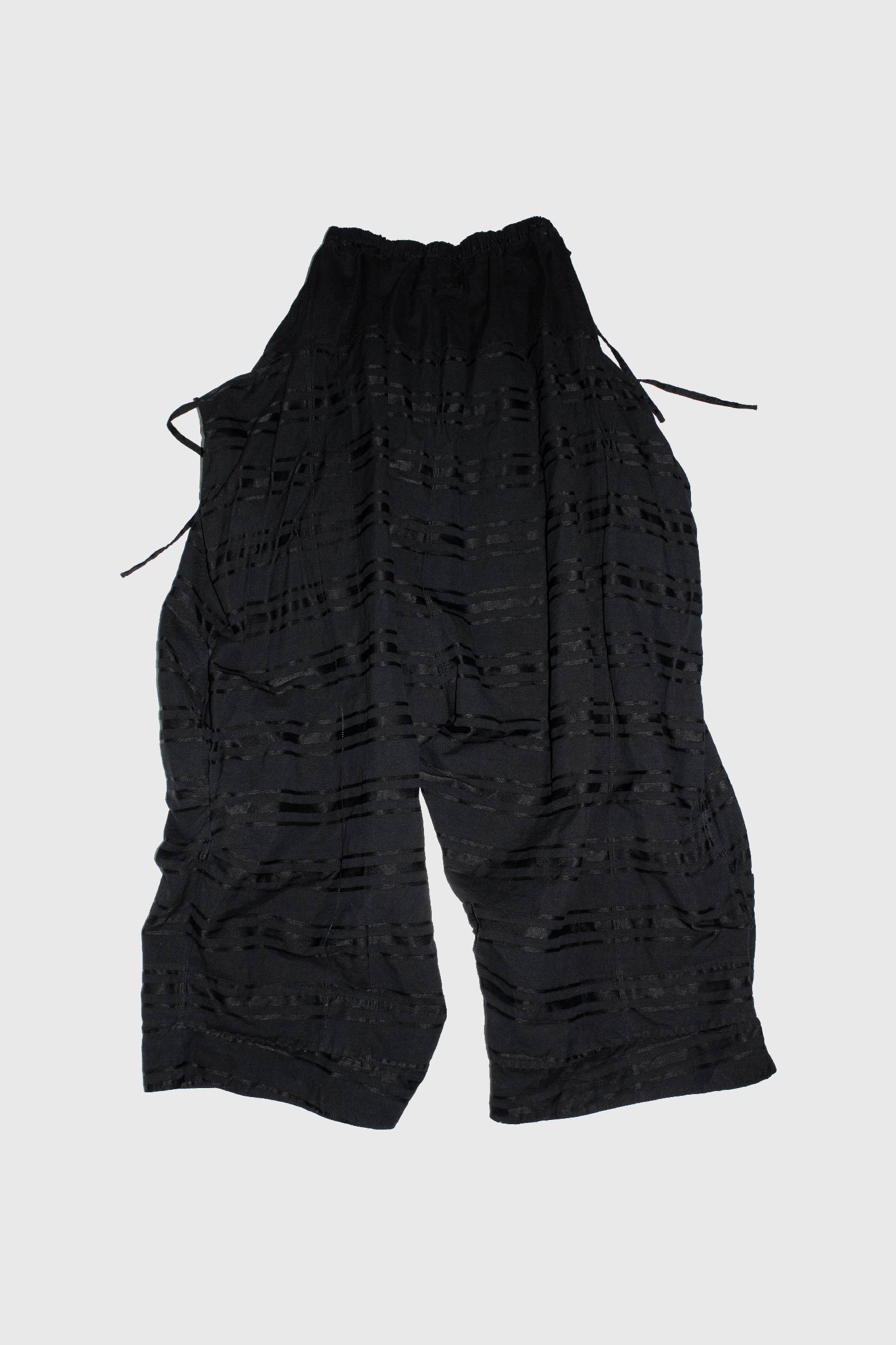Black striped trousers laid flat showing back view with drawcord details and manipulated stripe construction