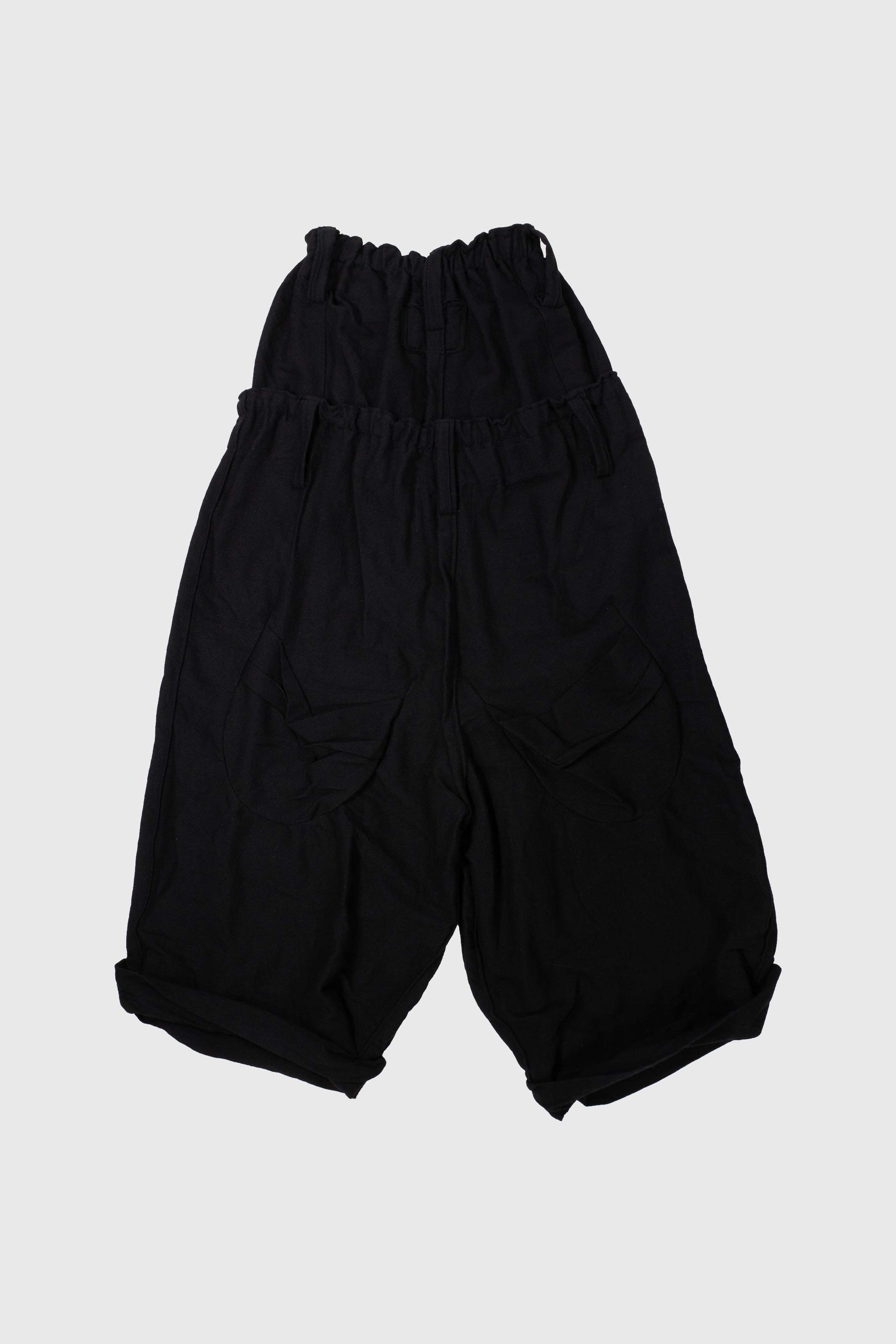 Front view of black wool trousers laid flat displaying double waist and cargo pocket design