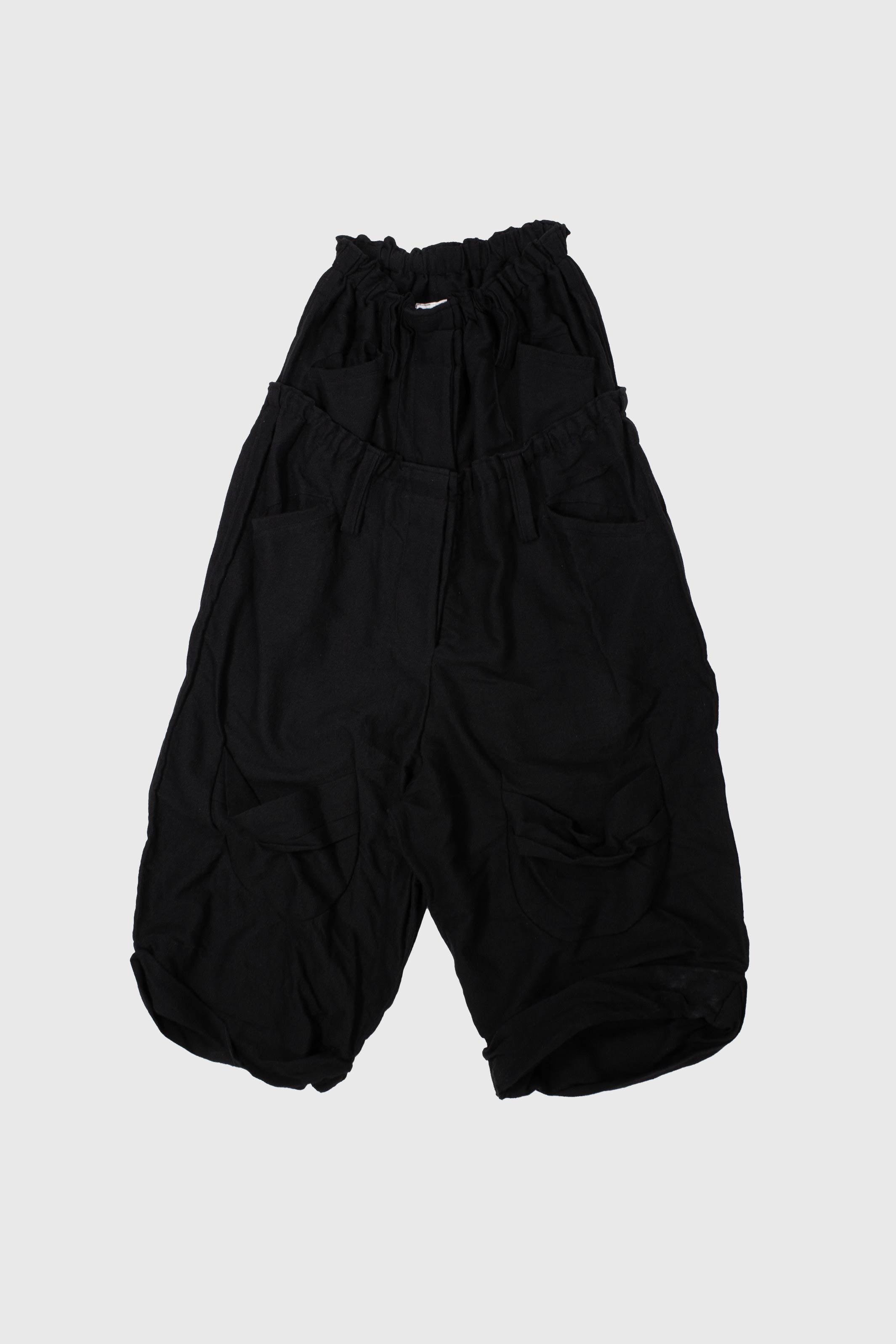 Black wool trousers laid flat showing double waistband construction and curved cargo pockets