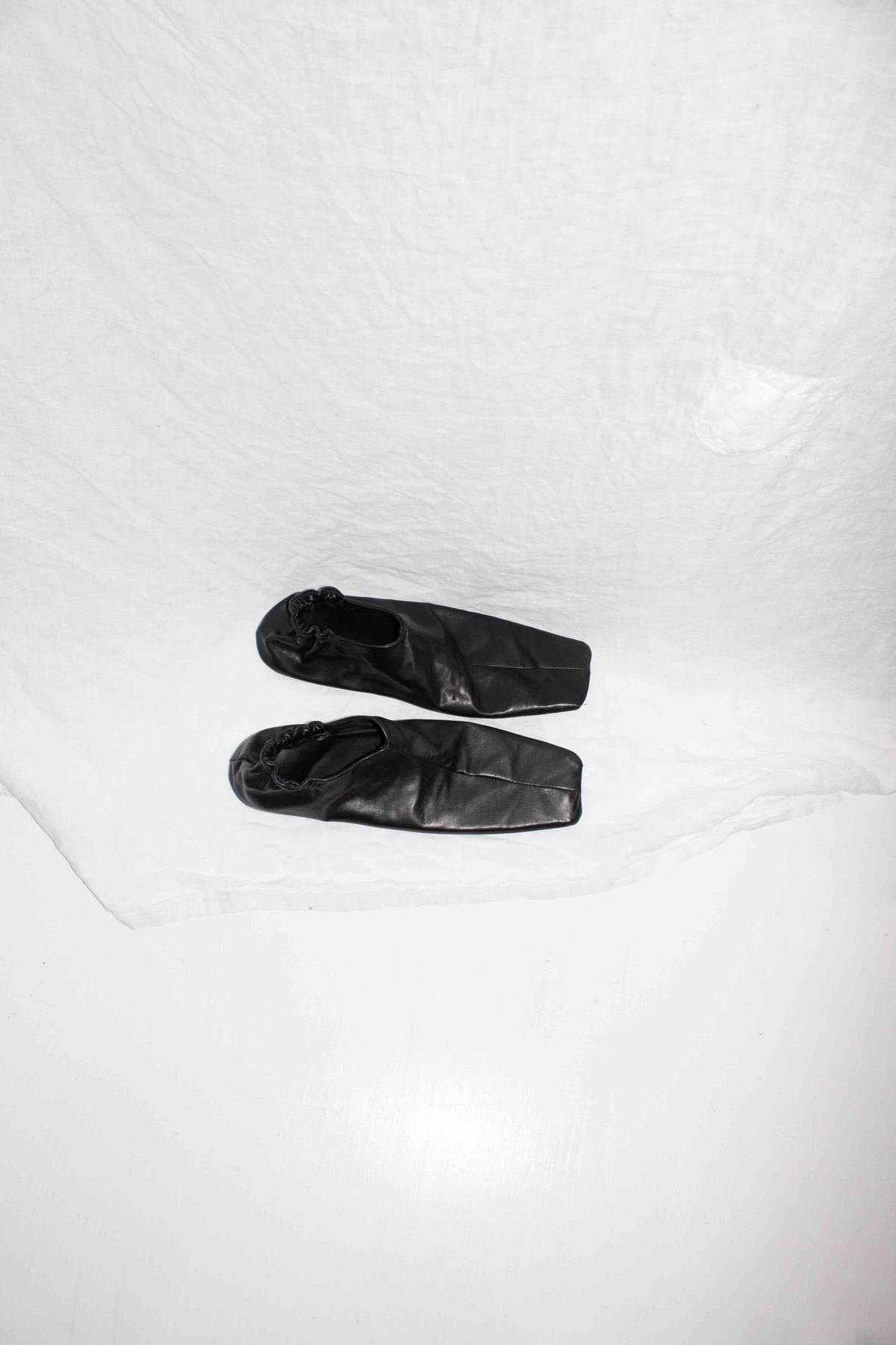 Black horse leather slip-on shoes with square toes positioned on white surface, top-down angle – Slip On Shoe by NELLY JOHANSSON