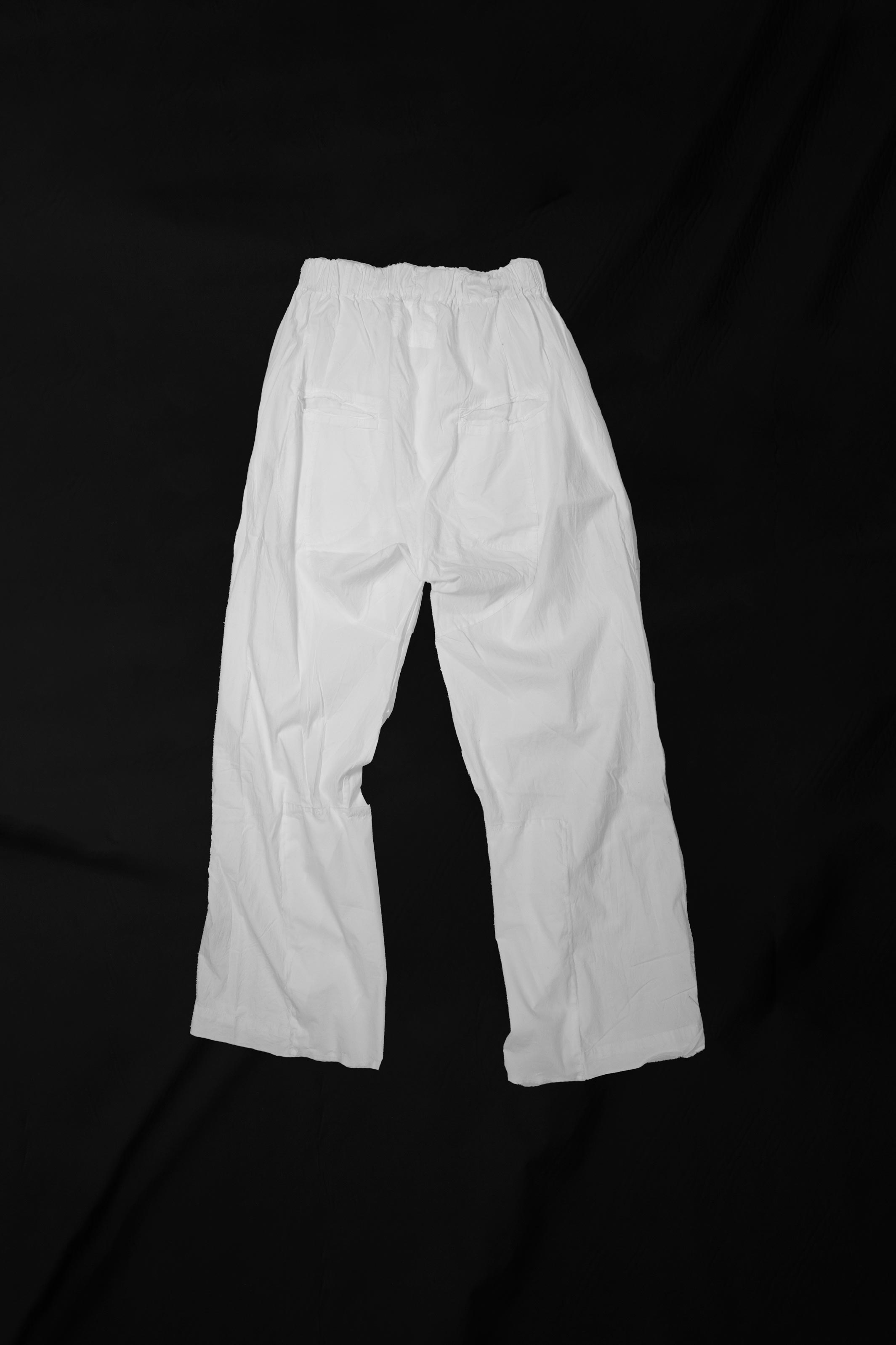 White loose slacks laid flat from front showing notched knee construction