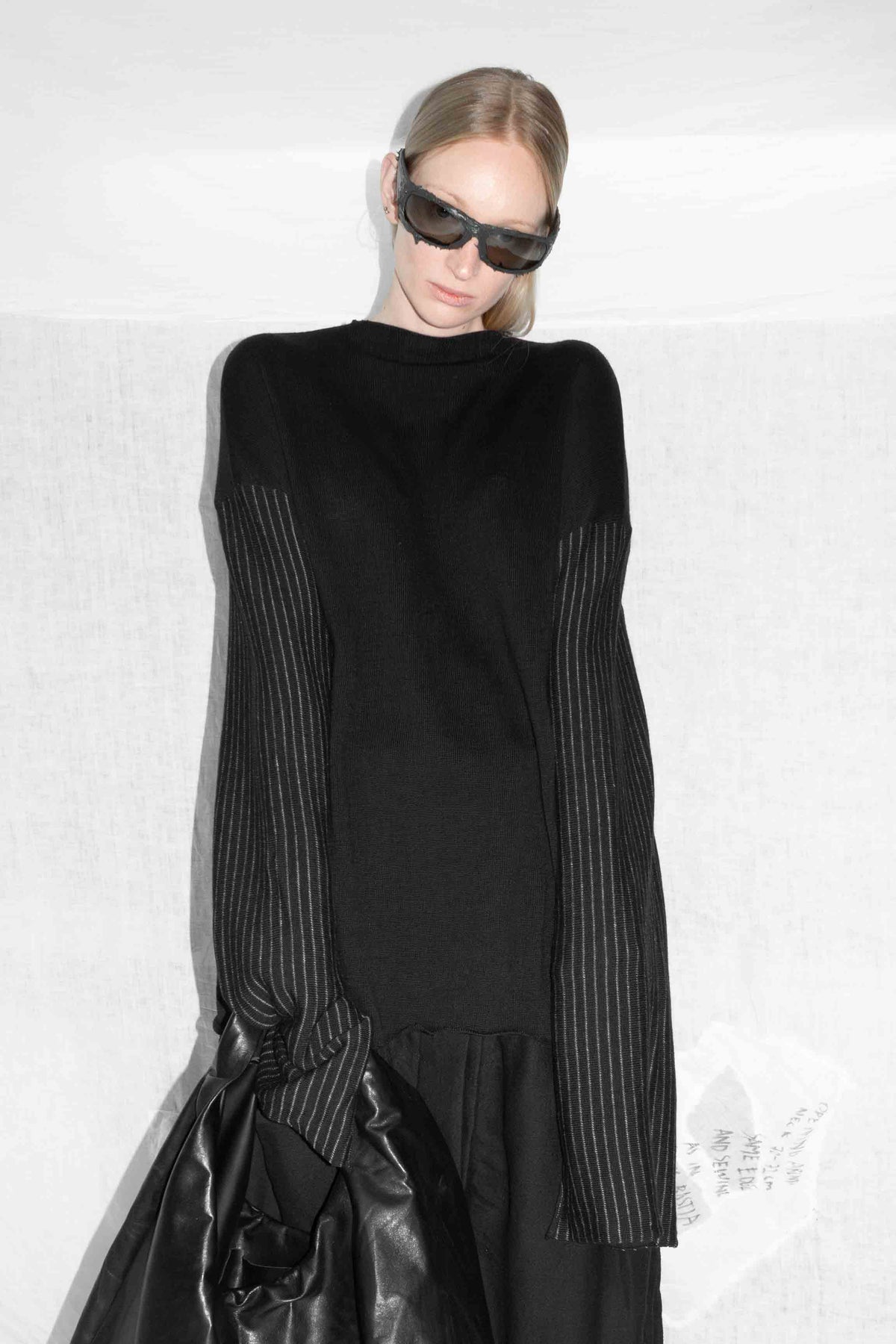 Model holding leather jacket while wearing black sweater with distinctive striped sleeves – Striped Sleeve Merino Wool Knit Sweater by NELLY JOHANSSON 3
