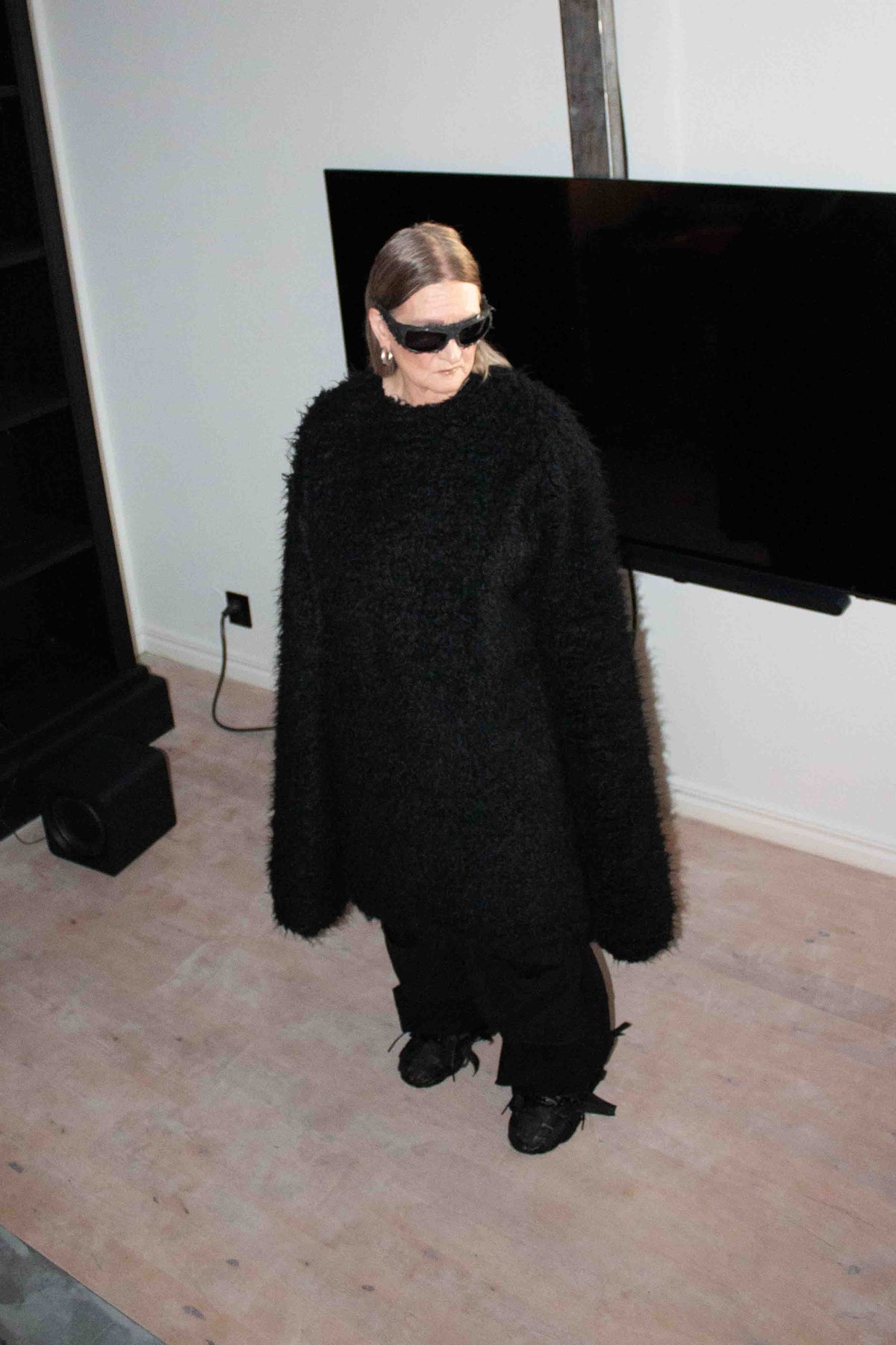 Nelly Johansson, founder and designer, in an oversized black coat and sunglasses in a sunlit apartment – NELLY JOHANSSON 2024–25