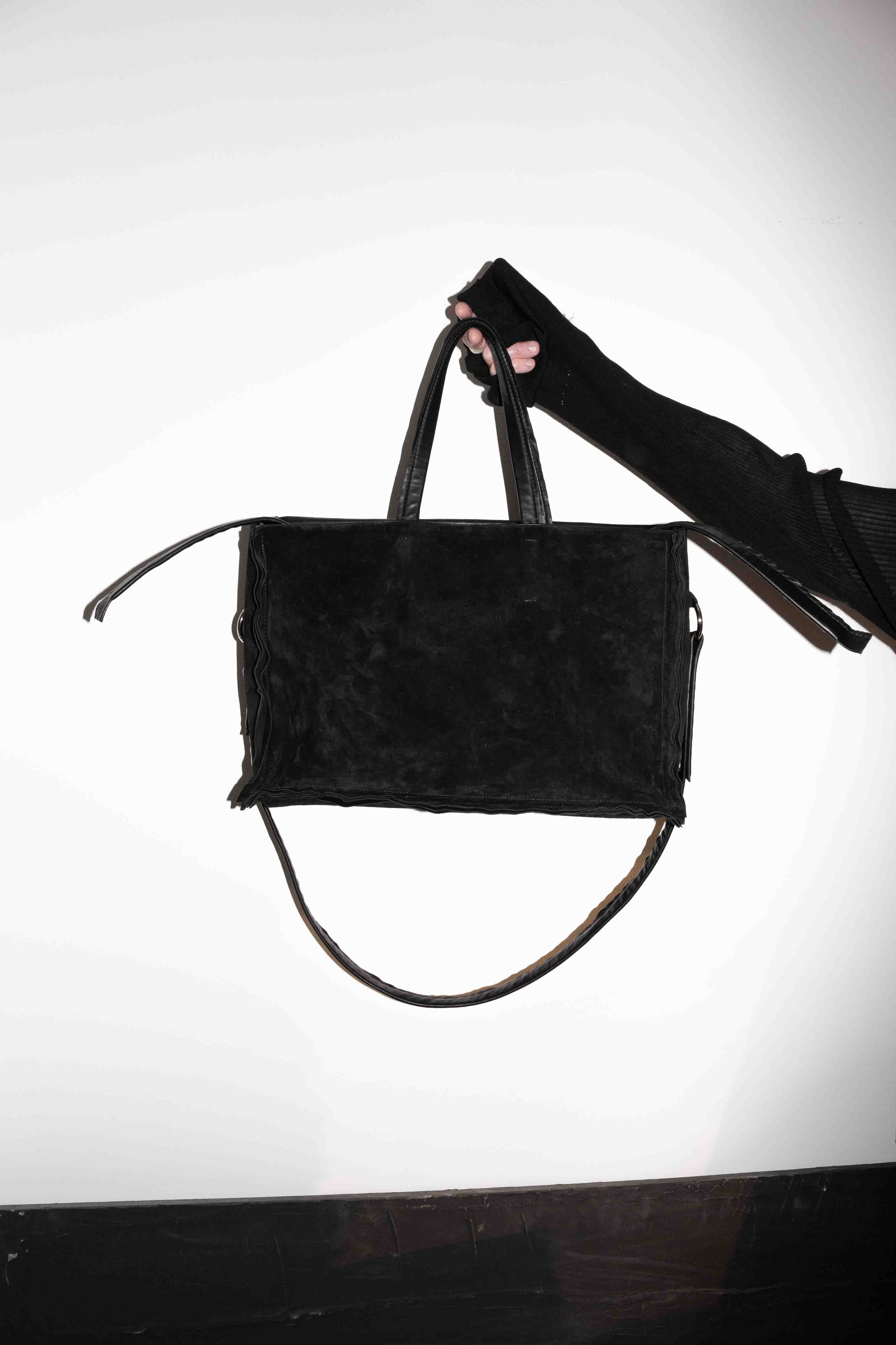 Hand holding black horse leather tote bag showing textured suede reverse side with frayed edges