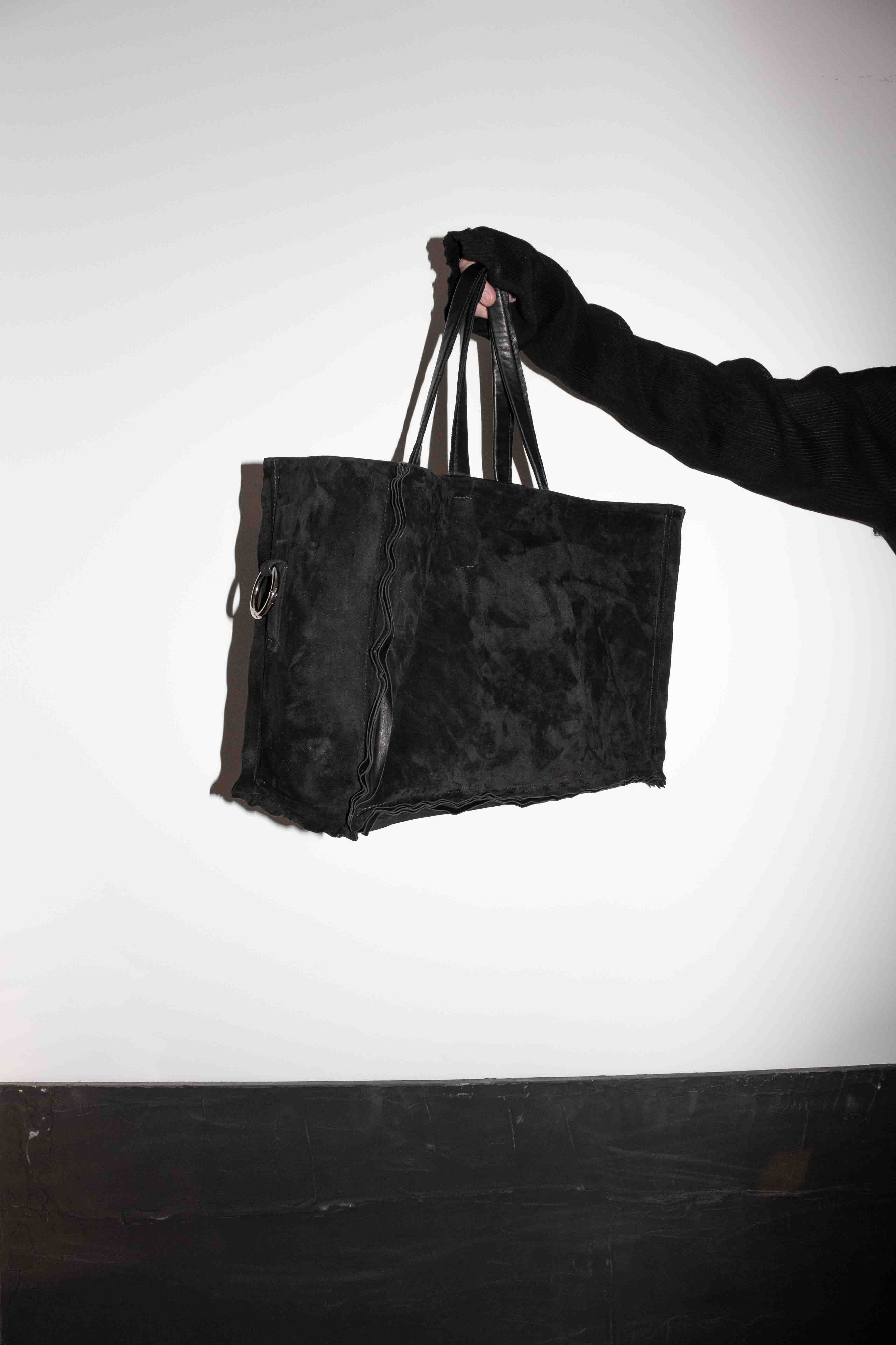 Hand holding horse leather tote bag from above showing raw edge suede construction and ring hardware