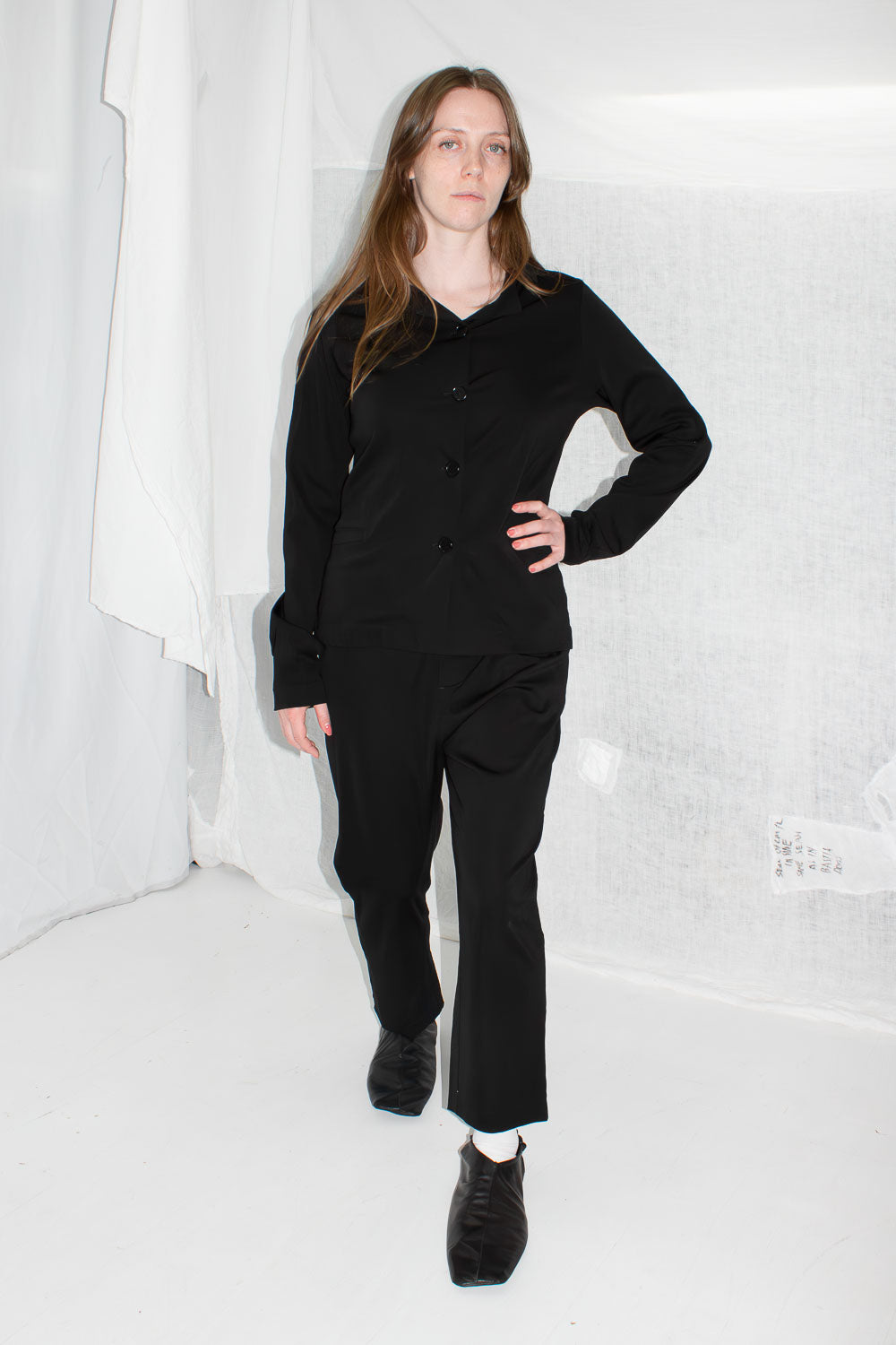 Model in black tailored jacket and trousers, front view showing asymmetrical collar detail and overall fit
