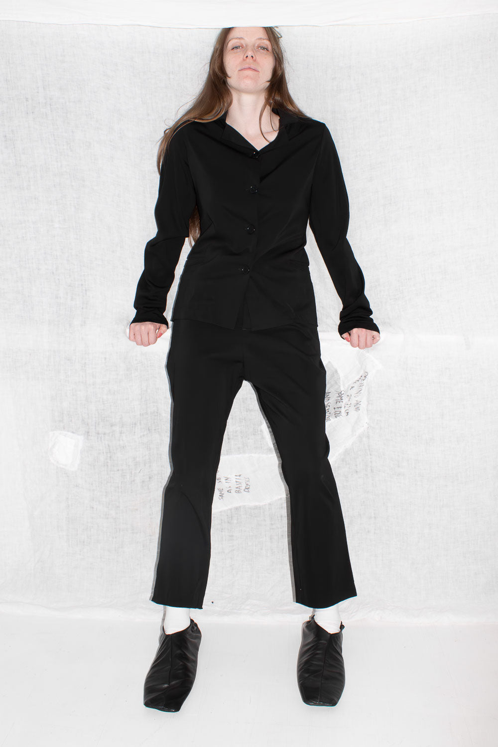 Model wearing black tailored jacket with matching trousers, showing fitted silhouette and button closure