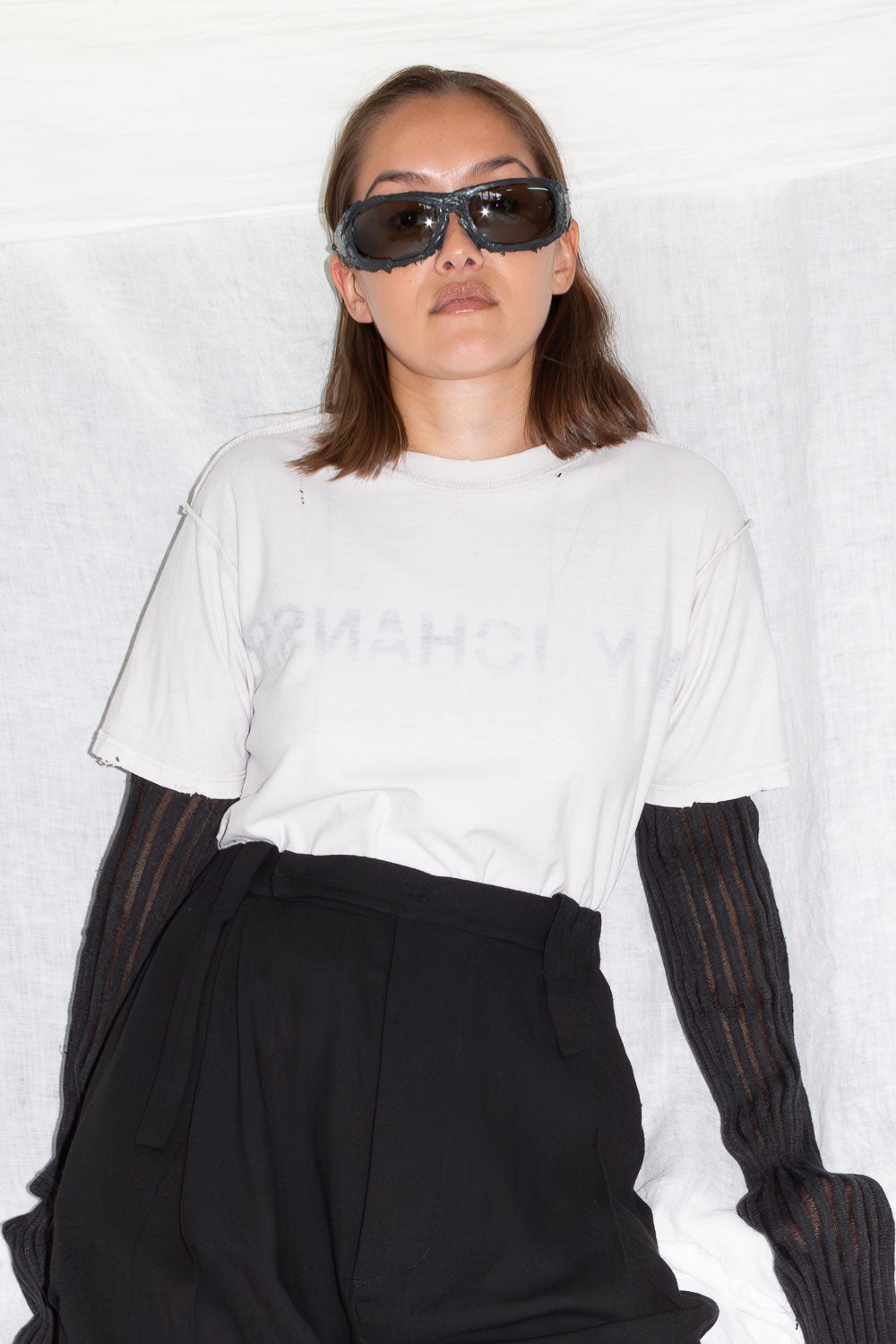 Model in sunglasses wearing white t-shirt with black sleeves underneath and black trousers