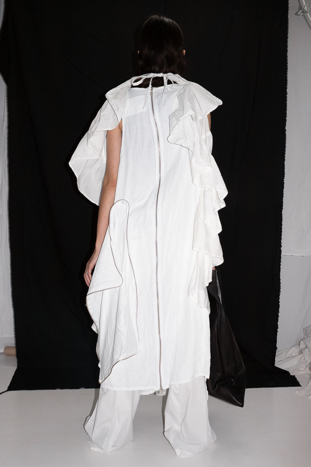 Back view of white ruffle dress showing metal zipper closure and asymmetric draping on model