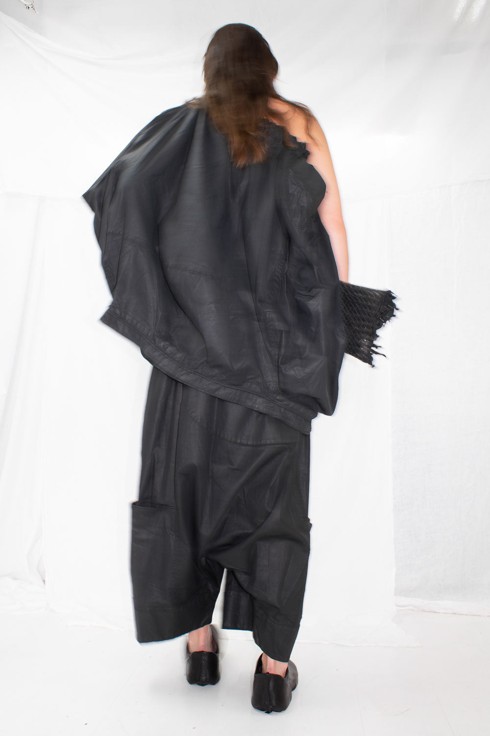 Back view of model in black sculptural trousers and oversized top with woven textured accessories