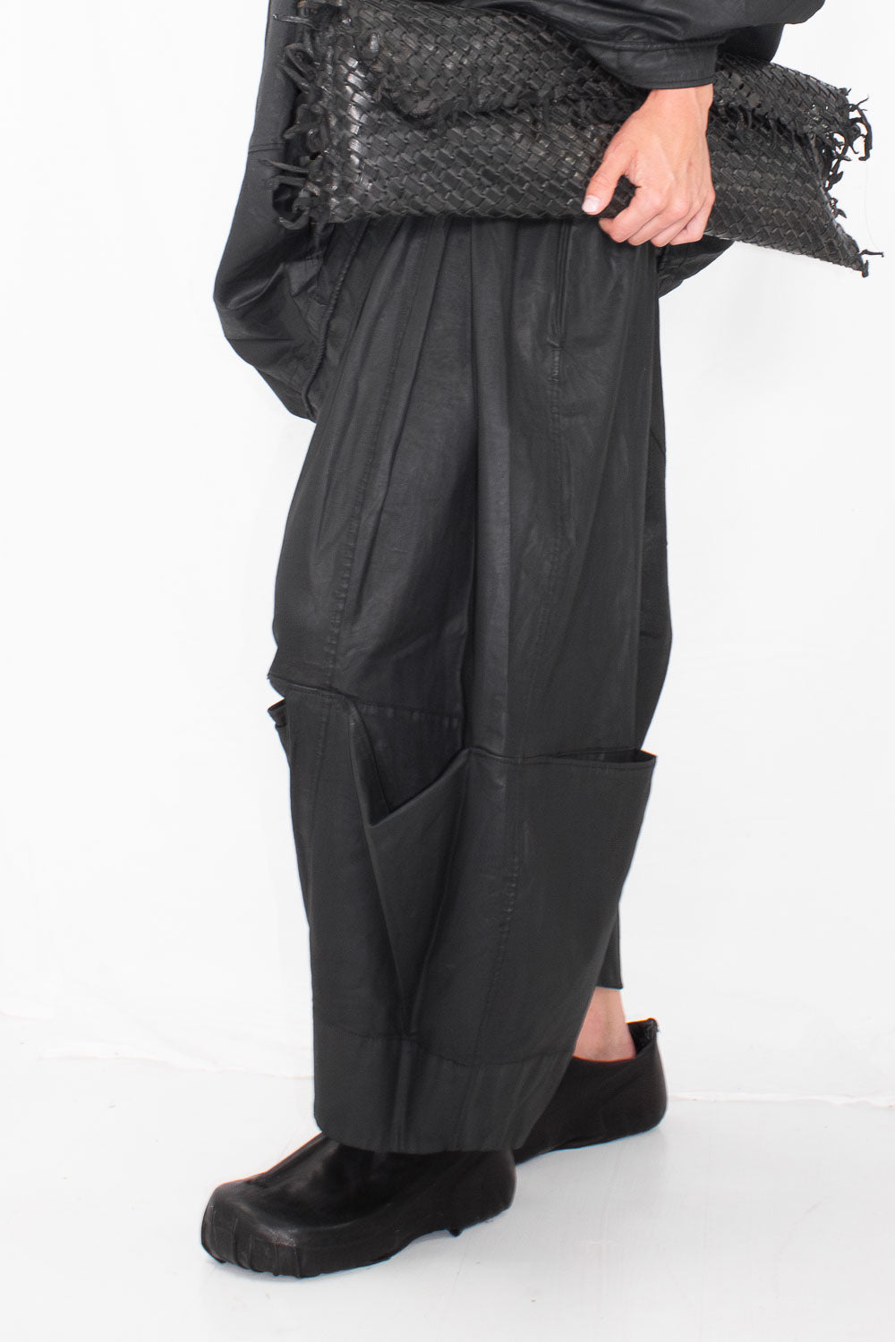 Side profile of model wearing black drop crotch trousers with visible pocket details