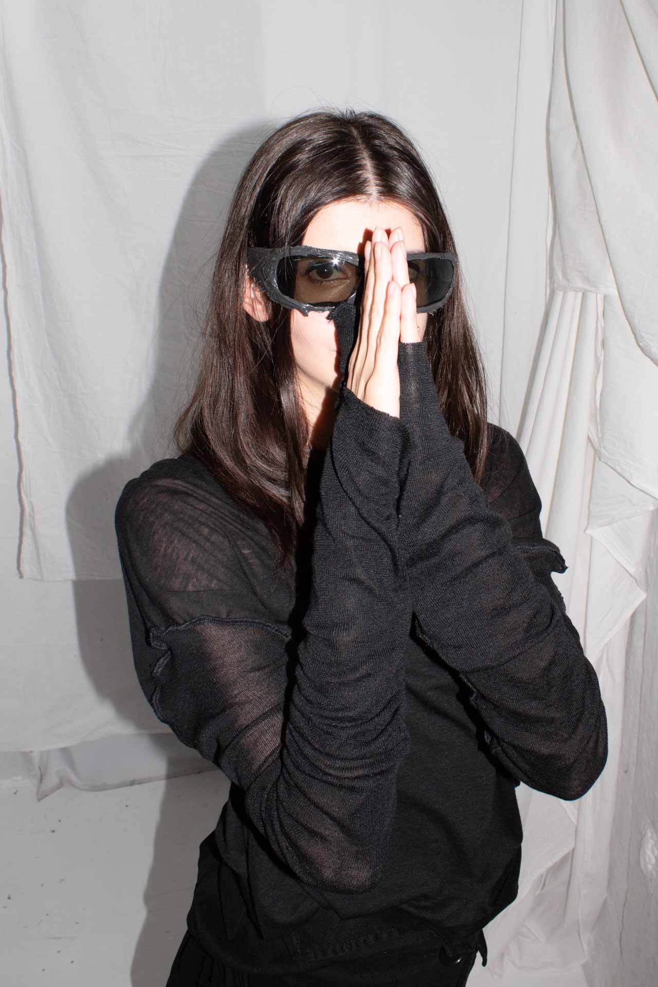 Model in sunglasses with hands positioned showing thumb openings in sleeves