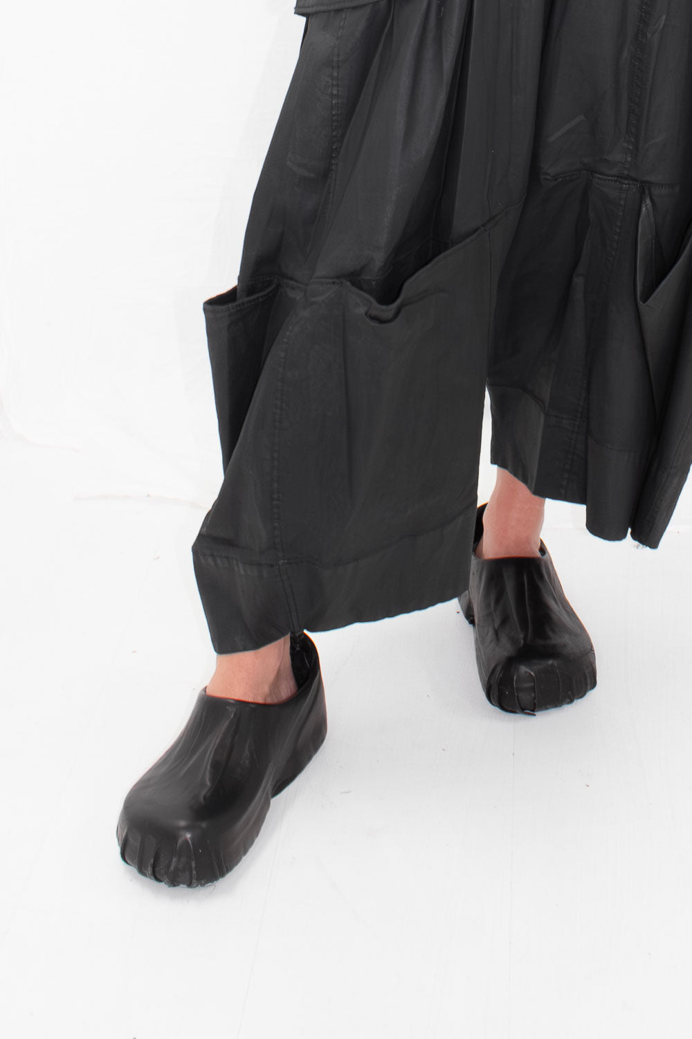 Model wearing black wrapped clogs with black flowing garments, side view