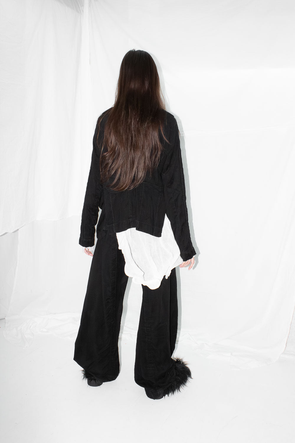 Model from behind wearing black jacket over the white shirt with long dark hair