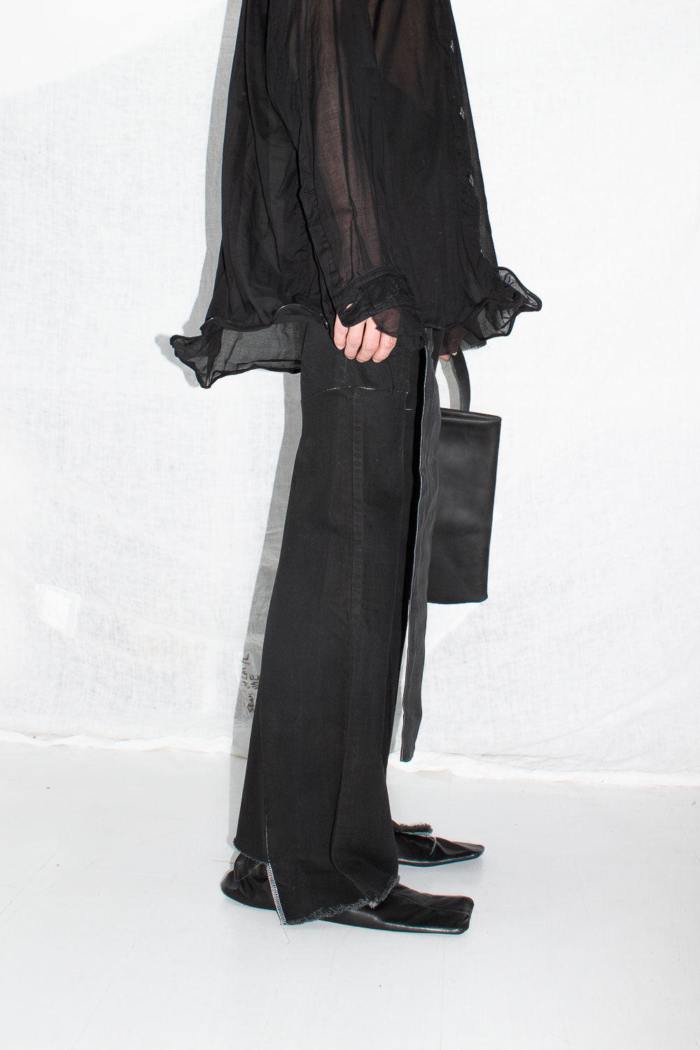 Close-up detail of model's hand holding black leather tote handle with black trousers visible