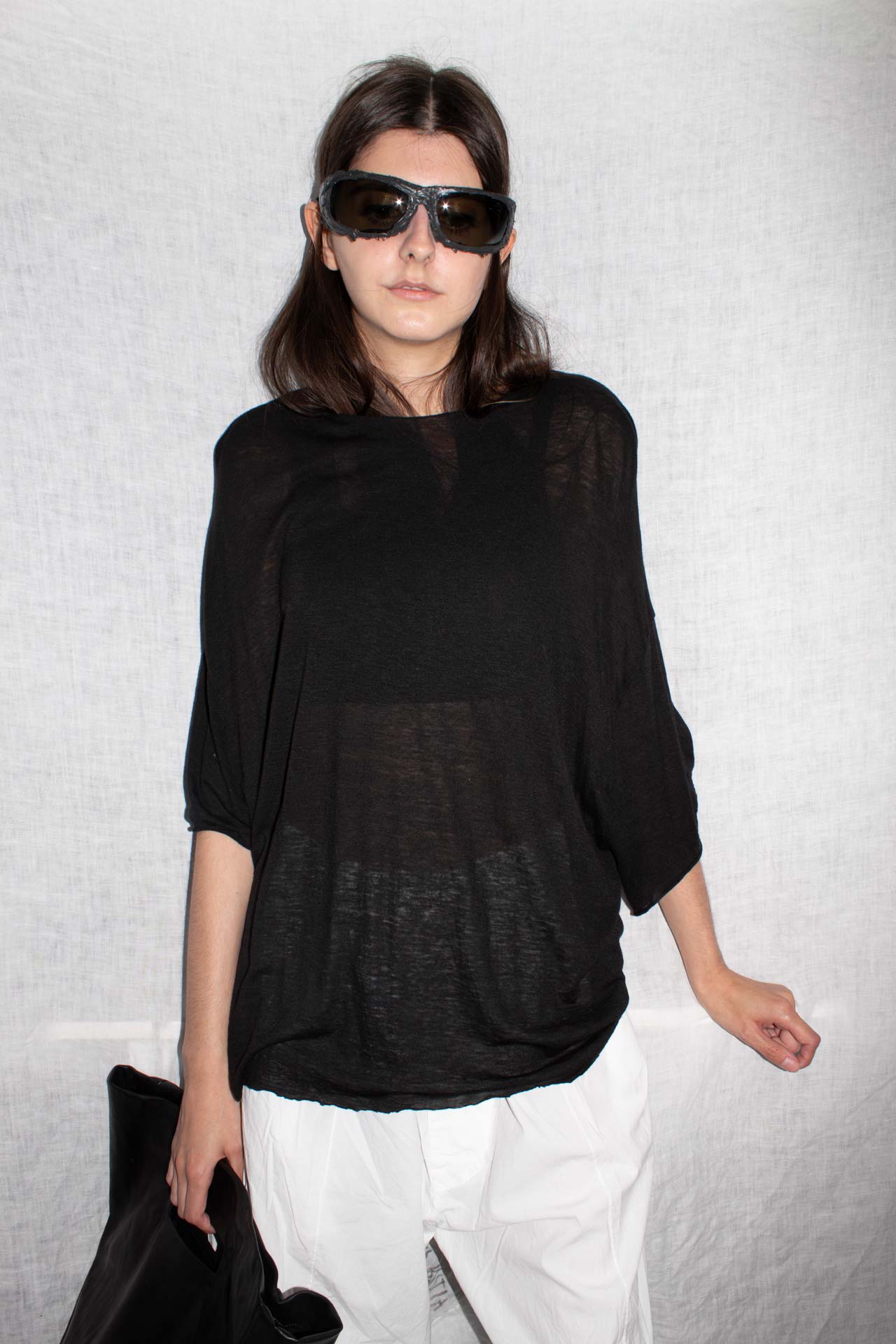 Model wearing oversized black t-shirt with dropped shoulders and cropped fit, styled with white trousers and sunglasses