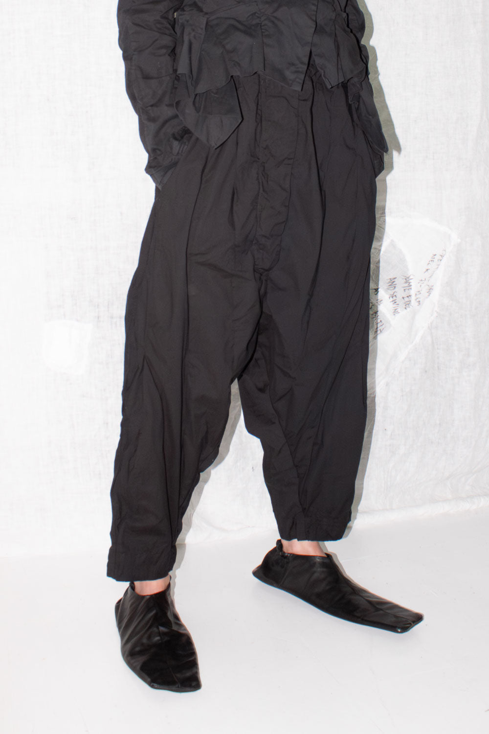 Front detail view of pleated trousers showing button fly and gathered waist construction